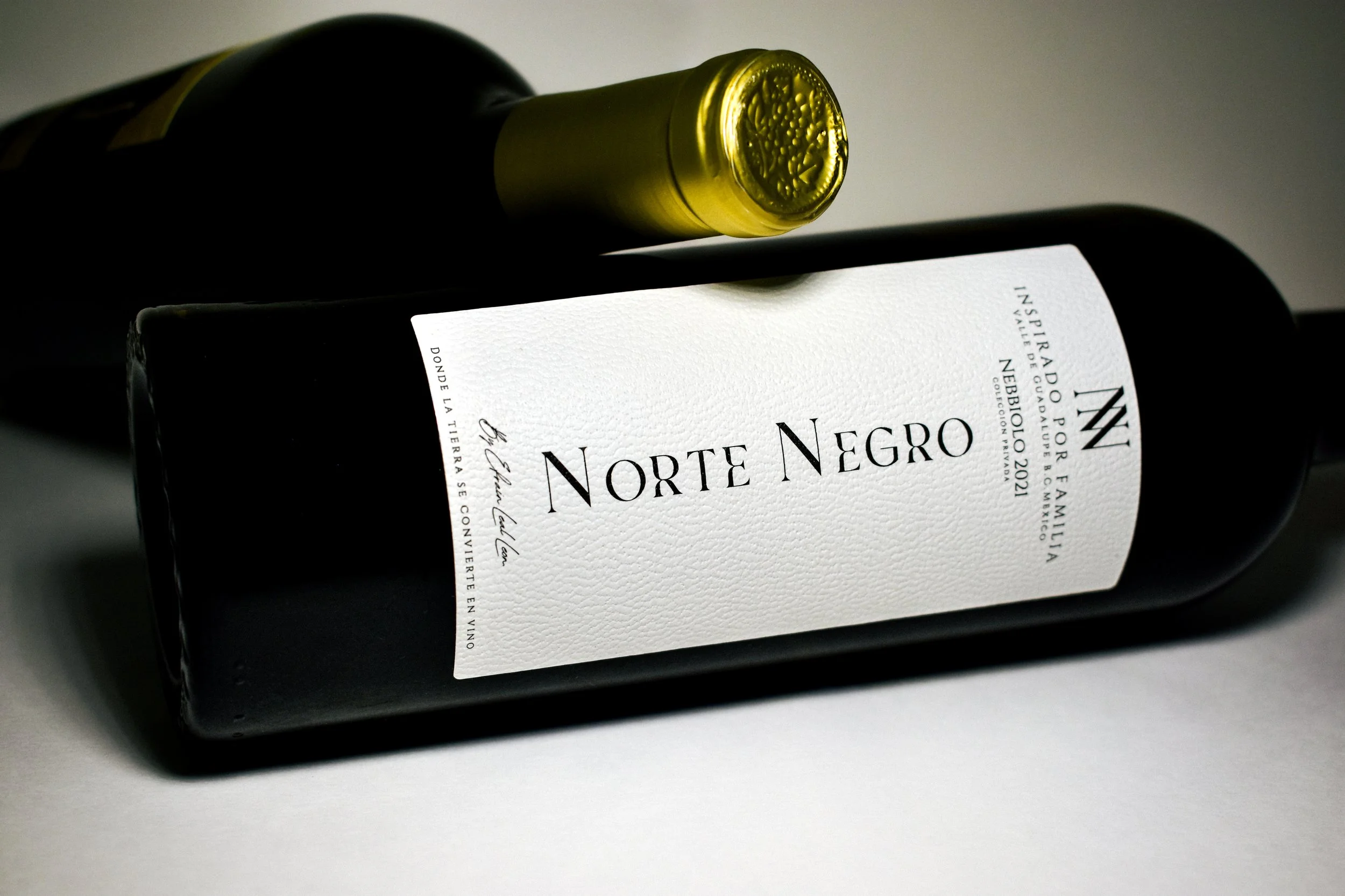 Botella de vino tinto etiquetada 'Norte Negro', con doble etiqueta blanca y letras negras, colocada en una superficie gris con un fondo oscuro.