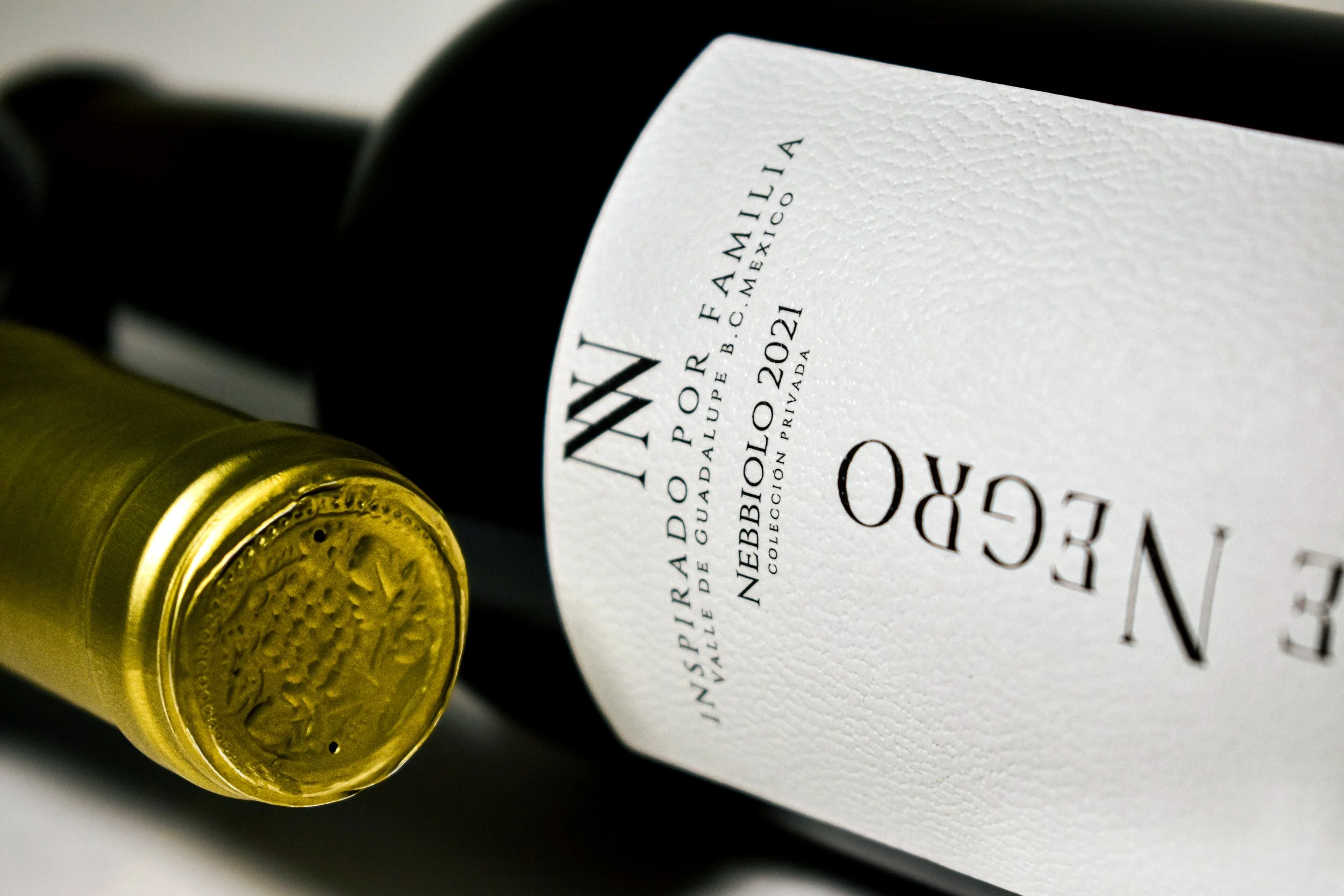 Botellas de vino tinto y vino espumoso en primer plano, uno con etiqueta blanca y letra negra, en un fondo oscuro.