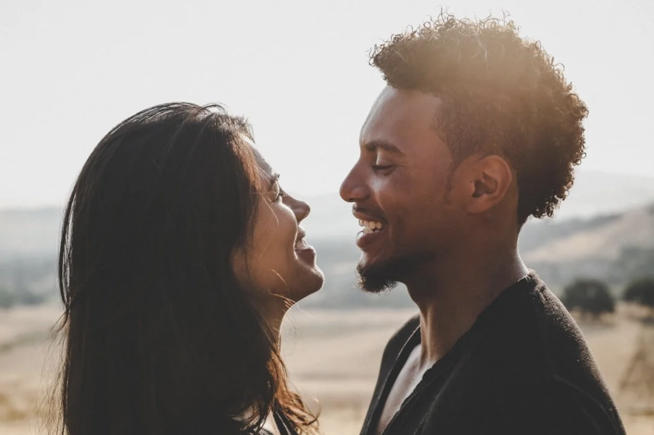 A smiling couple facing each other outdoors with a soft landscape behind them — representing the connection and hope that couples therapy can restore — Attune Therapy Group, Whidbey Island, Washington State