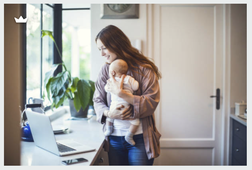 A mother holding her baby near a laptop in a bright home with a large window and green plant — representing how telehealth therapy with Attune Therapy Group makes support accessible for new parents throughout Seattle and Washington State, no babysitt