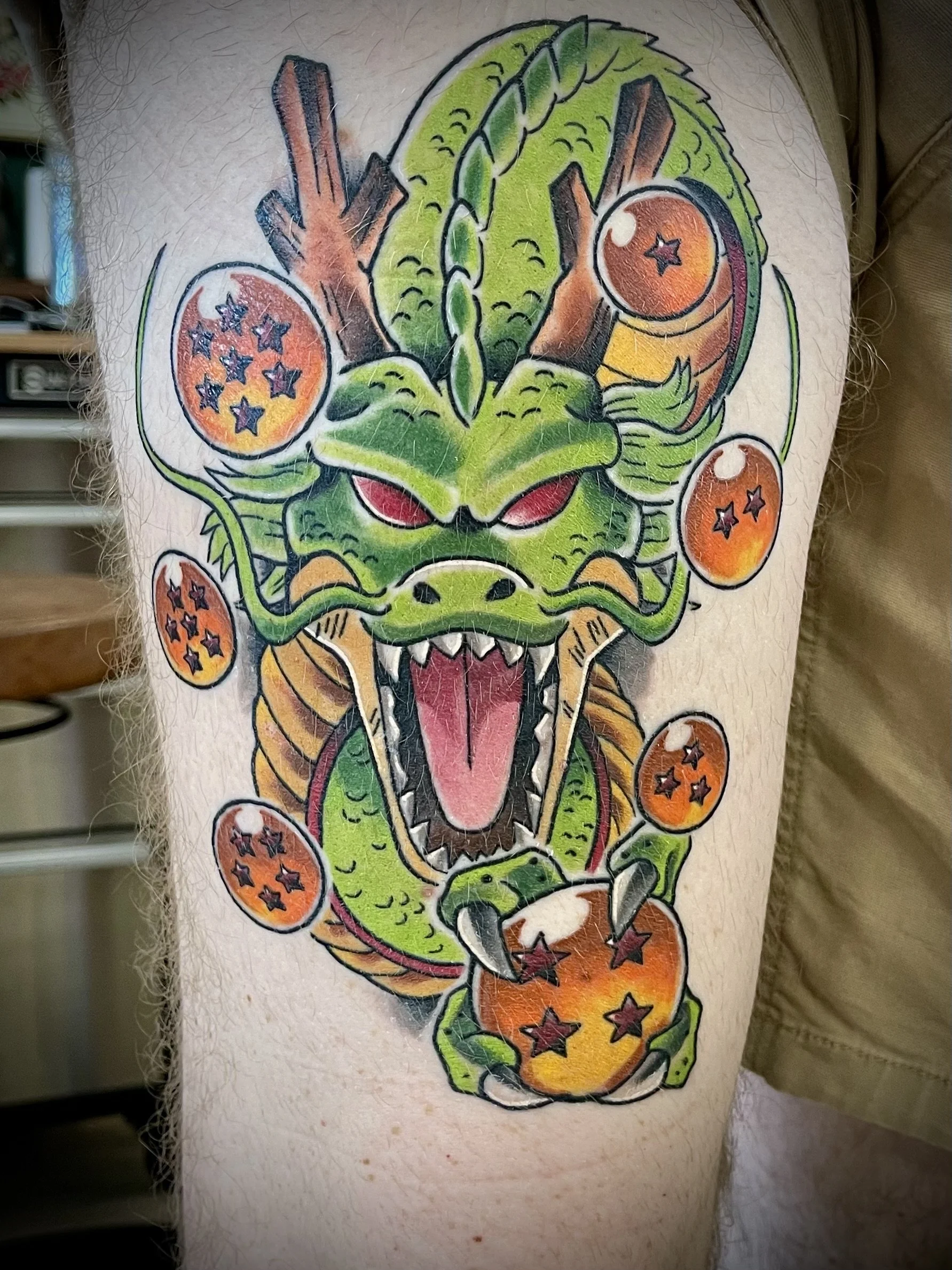 Colorful tattoo of a dragon's face on a person's skin, featuring green scales, red eyes, and sharp teeth.