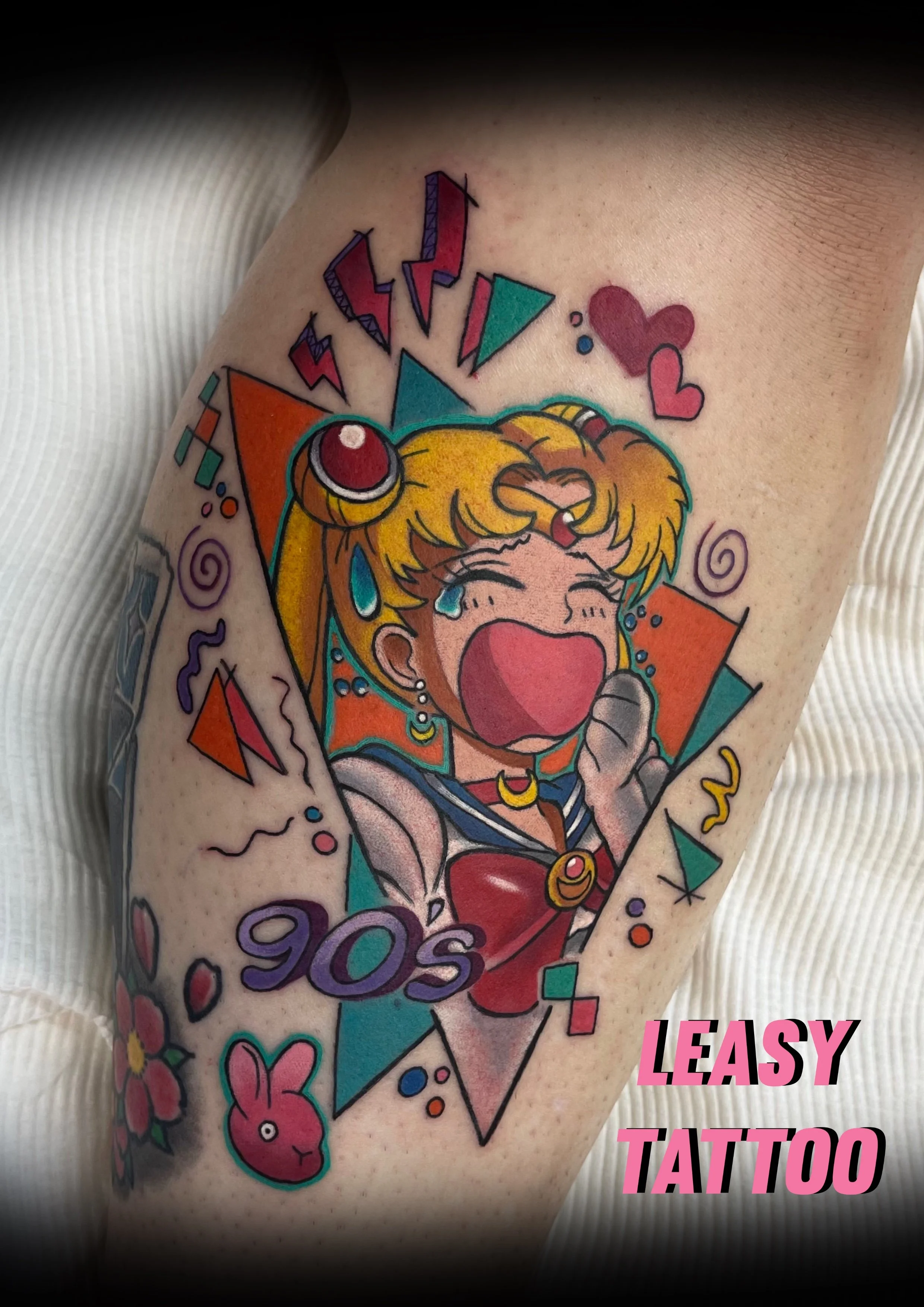 Colorful tattoo of Sailor Moon character with tears, surrounded by hearts, geometric shapes, and flowers, with pink text reading 'EASY TATTOO'.