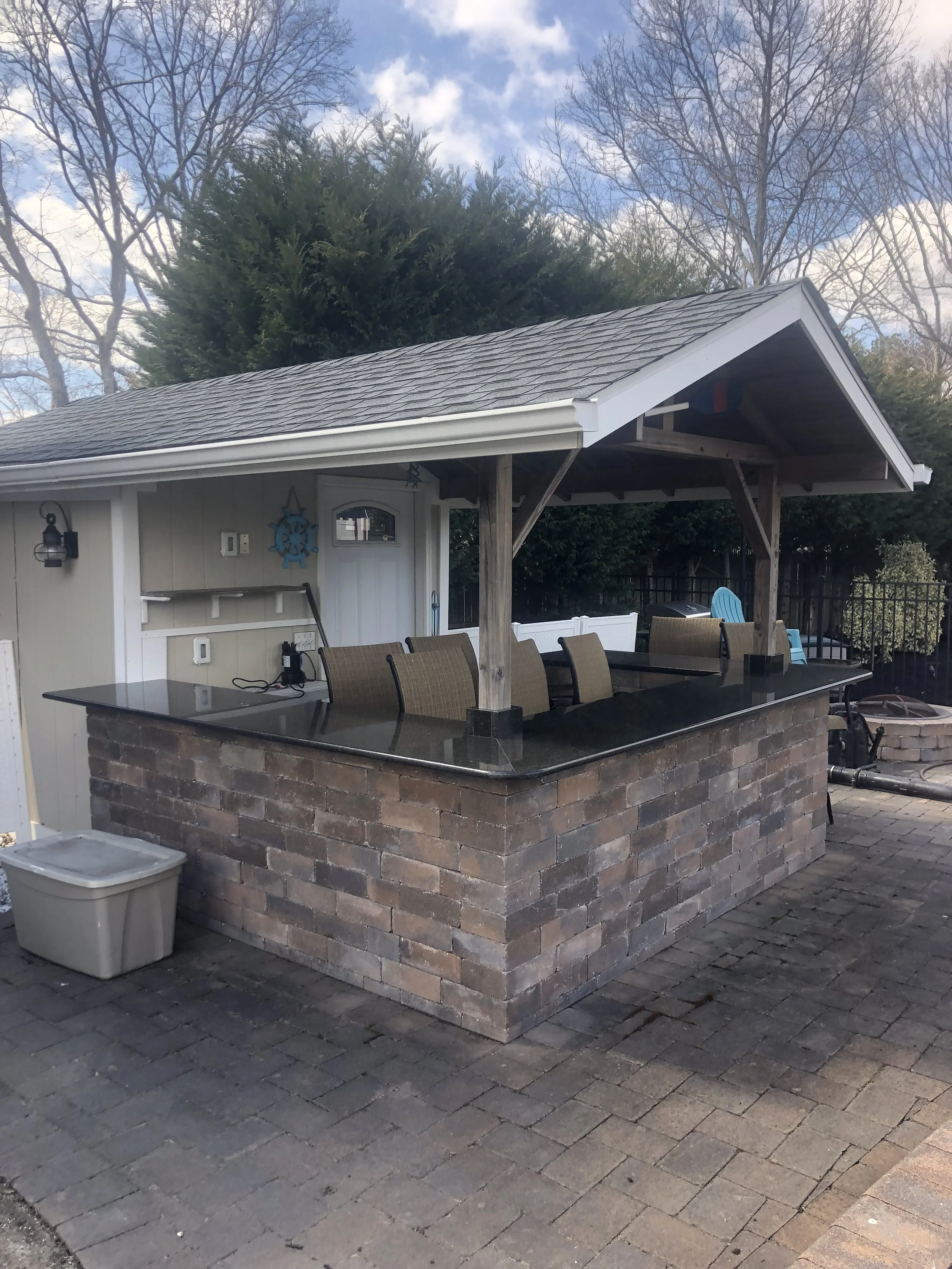 Outdoor built-in bar with a black granite countertop, supported by brick base and wooden posts, situated in a backyard.