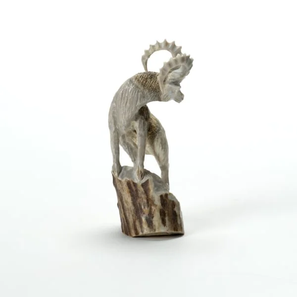 Wooden sculpture of a mountain goat standing on a rock, with curved horns and detailed fur.