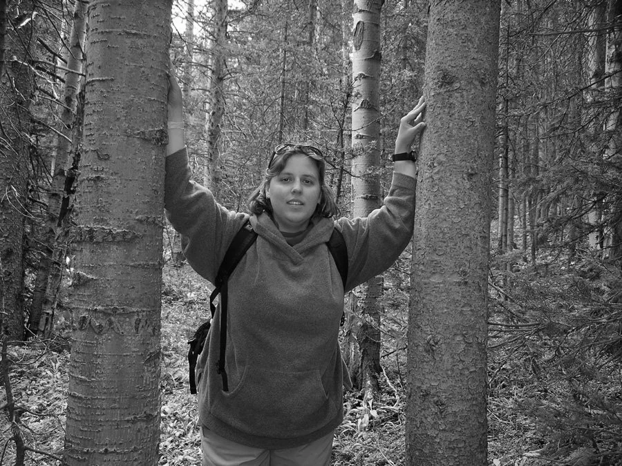 Claire standing between trees in a forest.