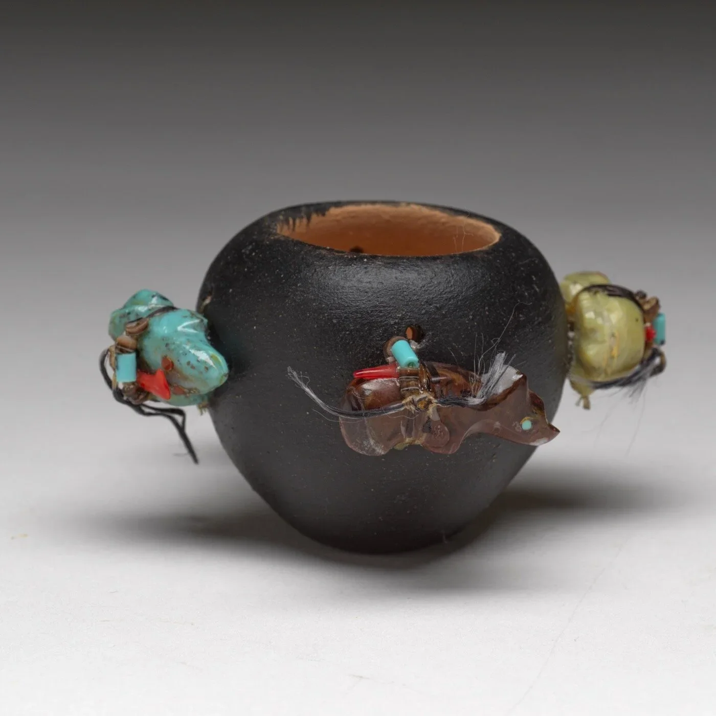 Edna Leki's Fetish Pot. A black ceramic vase with a wide opening, decorated with colorful, irregularly shaped beads and wire wrapped around it.