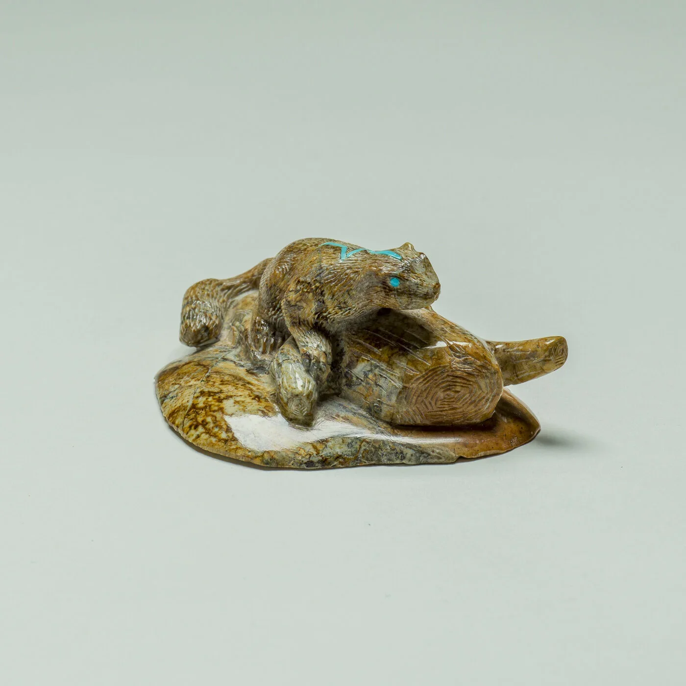 A small sculpture of a frog sitting on a rock, made from various types of wood with detailed textures and painted blue eyes.