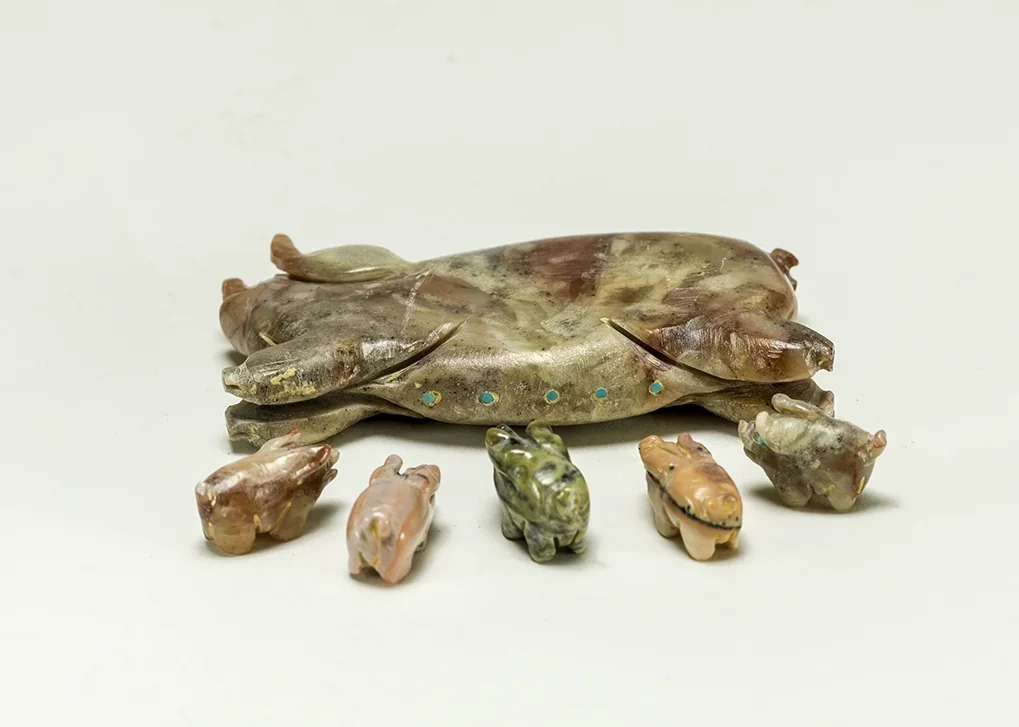 Five small carved frogs are arranged in front of a larger carved frog on a white background.