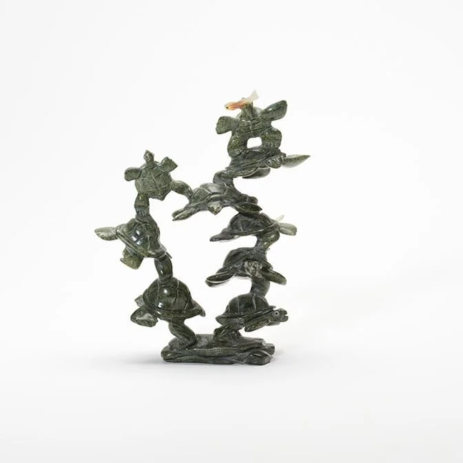 A sculpture of multiple turtles stacked on top of each other with a small fish on top, set against a plain white background.