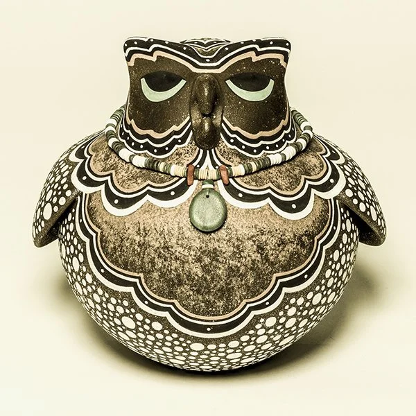 Decorative Zuni owl-shaped ceramic vessel with black, white, and brown patterns and a green pendant necklace.