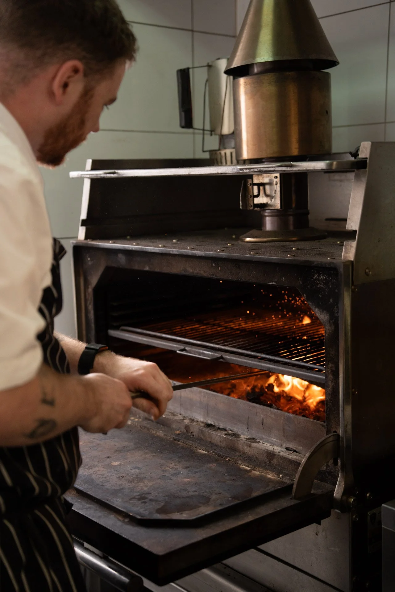 Albury greek best restaurant: A chef tending a wood-fired pizza oven with flames inside, adjusting a pizza peel.