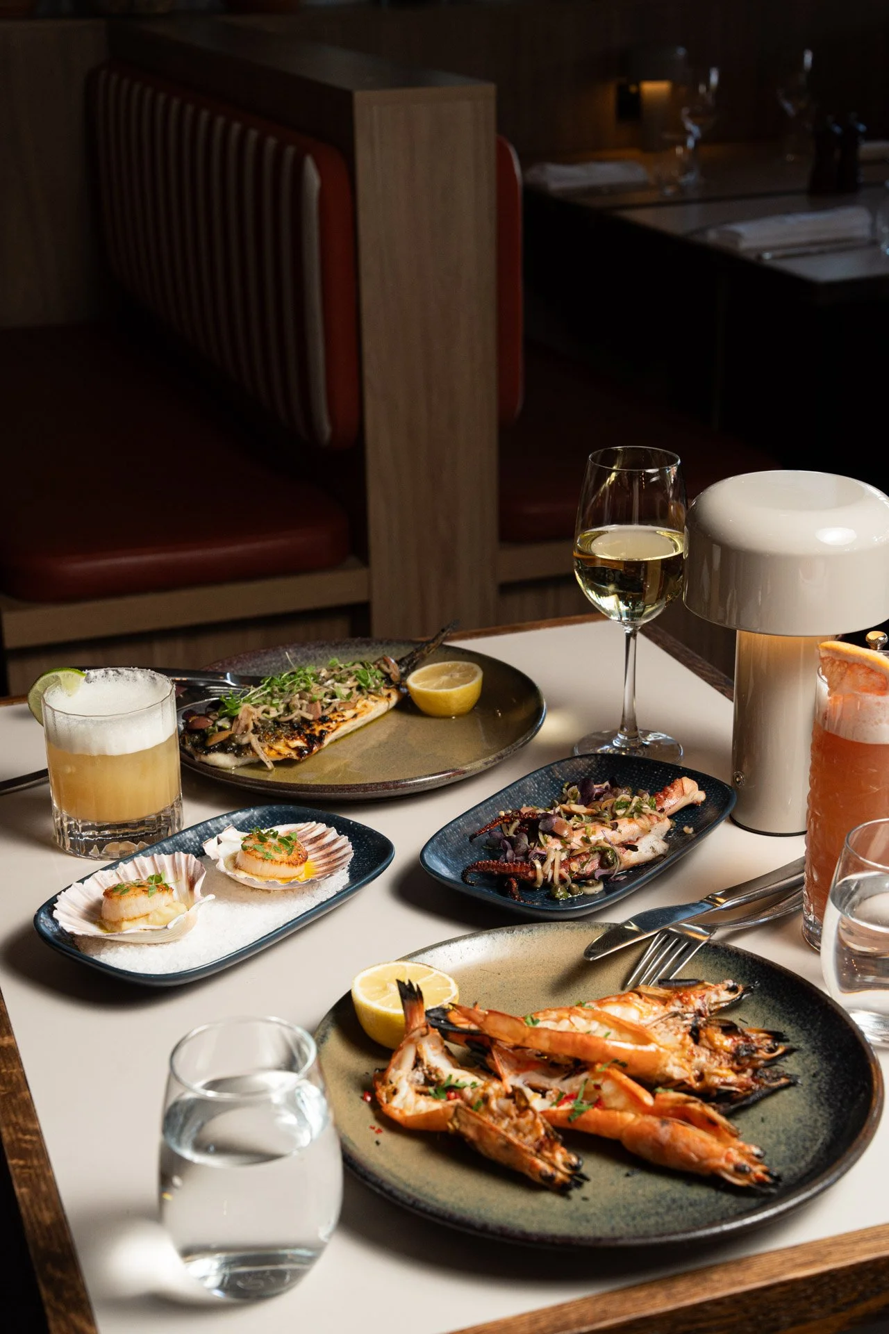 Albury greek best restaurant: A table set with various seafood dishes, including grilled shrimp, grilled fish, and squid, along with glasses of white wine and water, in a restaurant setting.