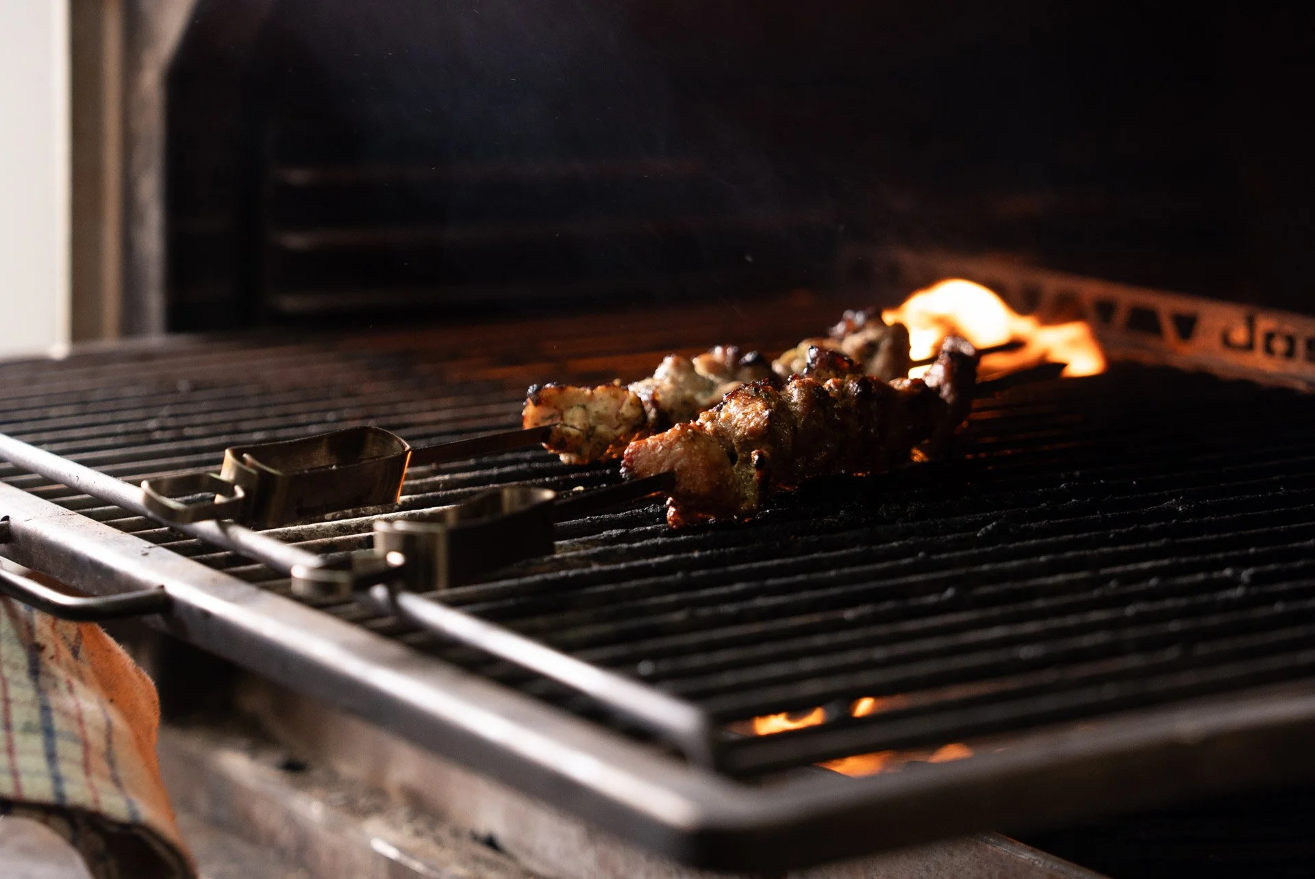 Albury greek best restaurant: Meat being grilled on an open flame barbecue grill with flames visible in the background.