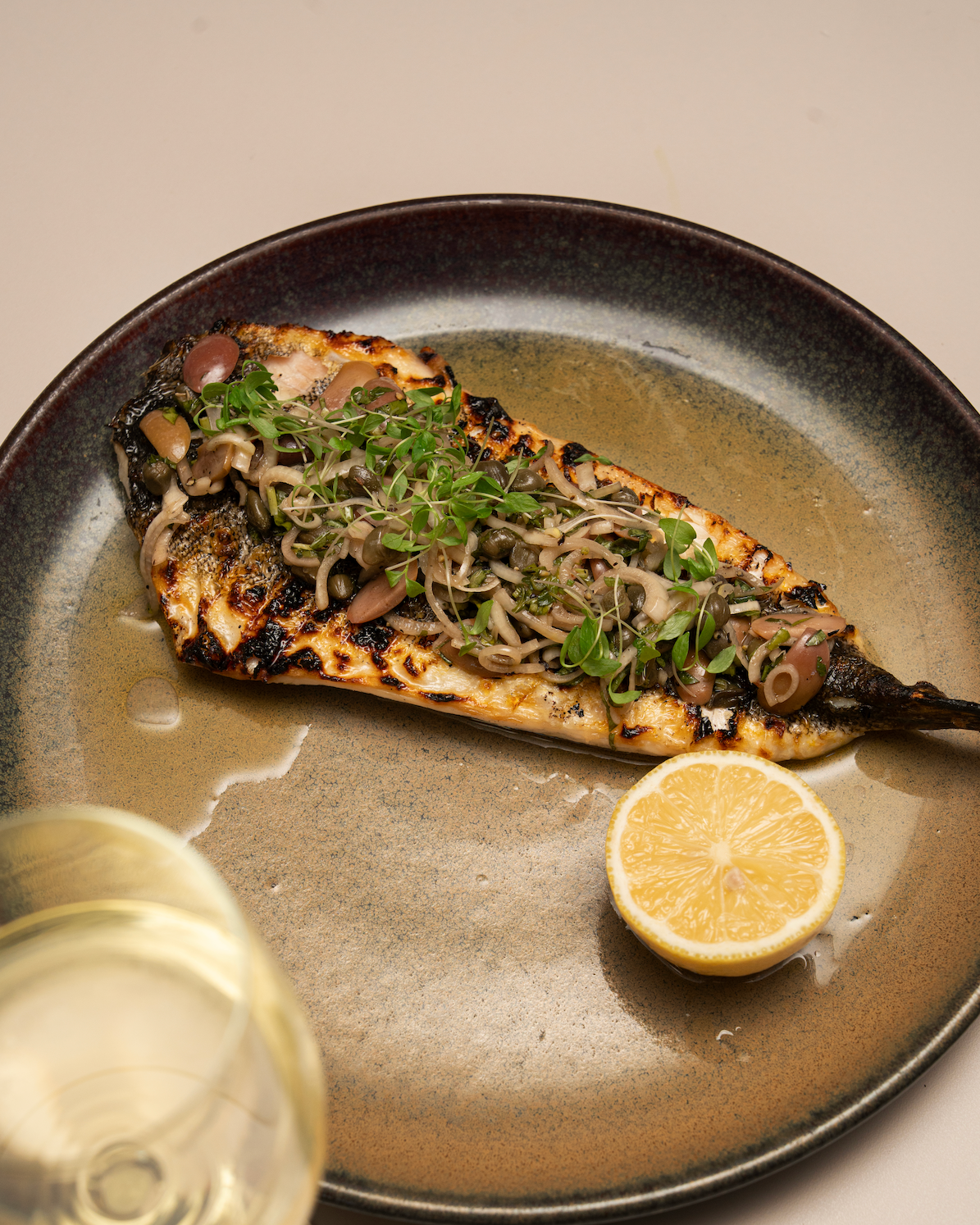 Albury greek best restaurant: Grilled fish fillet topped with a mix of greens, microgreens, and mushrooms, served with a lemon half and a glass of white wine.