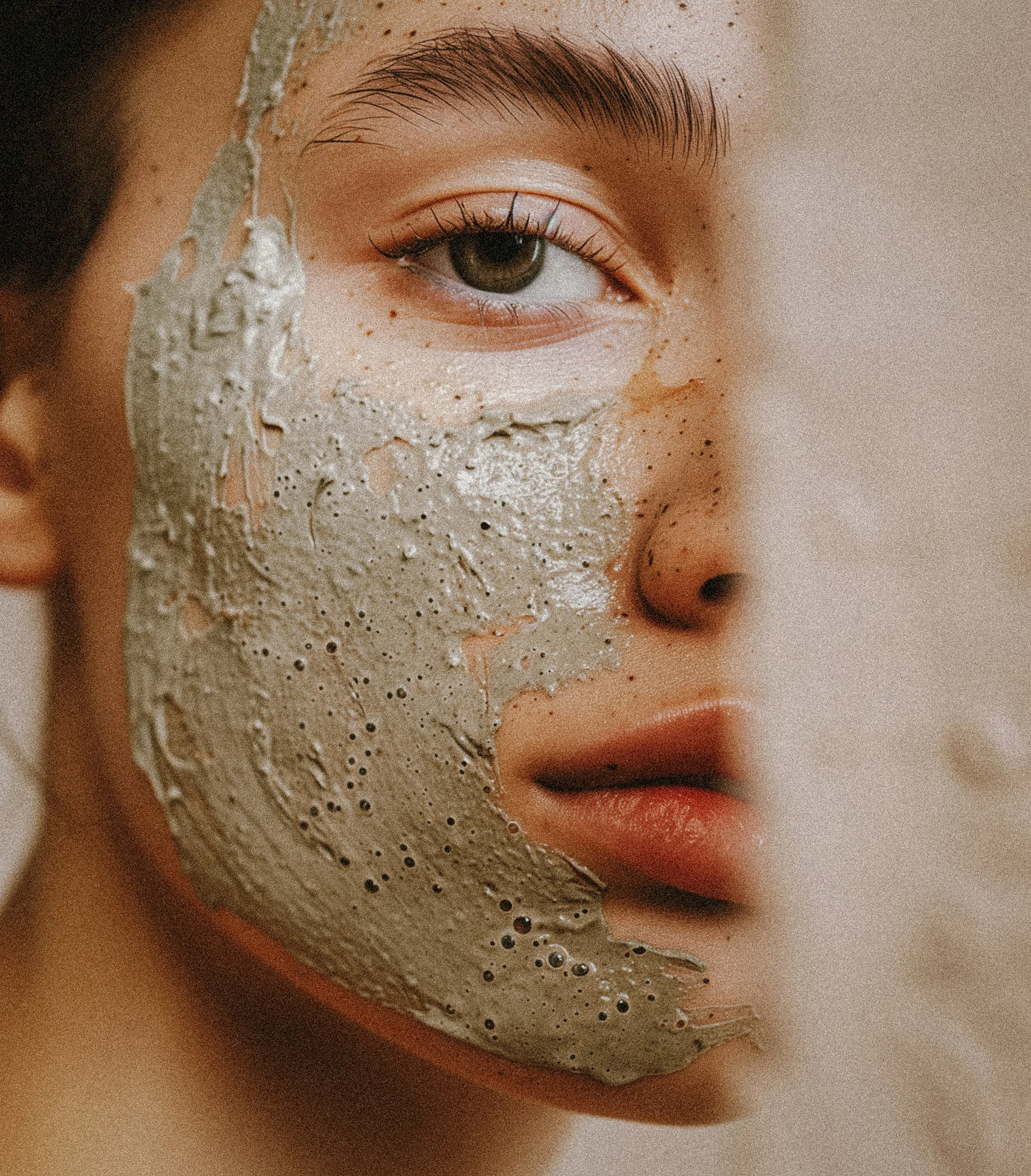 Close-up of a person's face with a creamy facial mask applied, focusing on one eye, eyebrow, and lips, with skin details and Freckles.