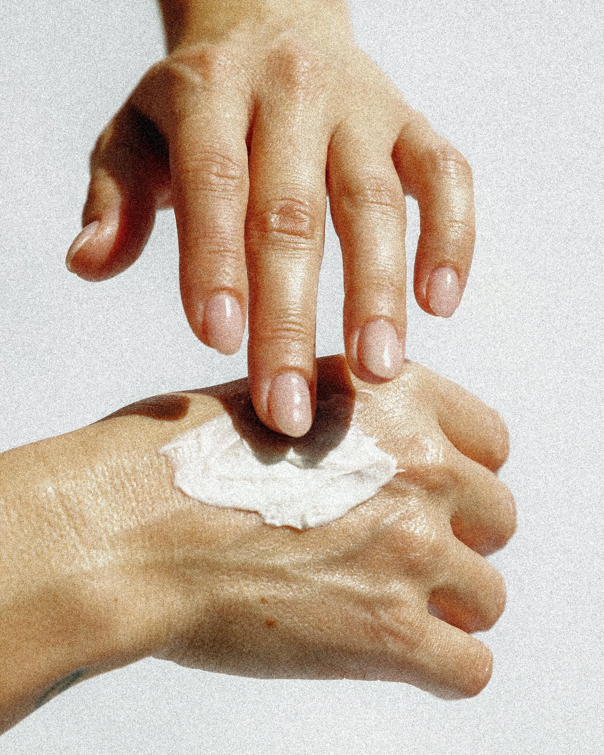 Close-up of a person applying or holding a white facial mask or retreat mask while their hand is visible. The background is plain and out of focus.