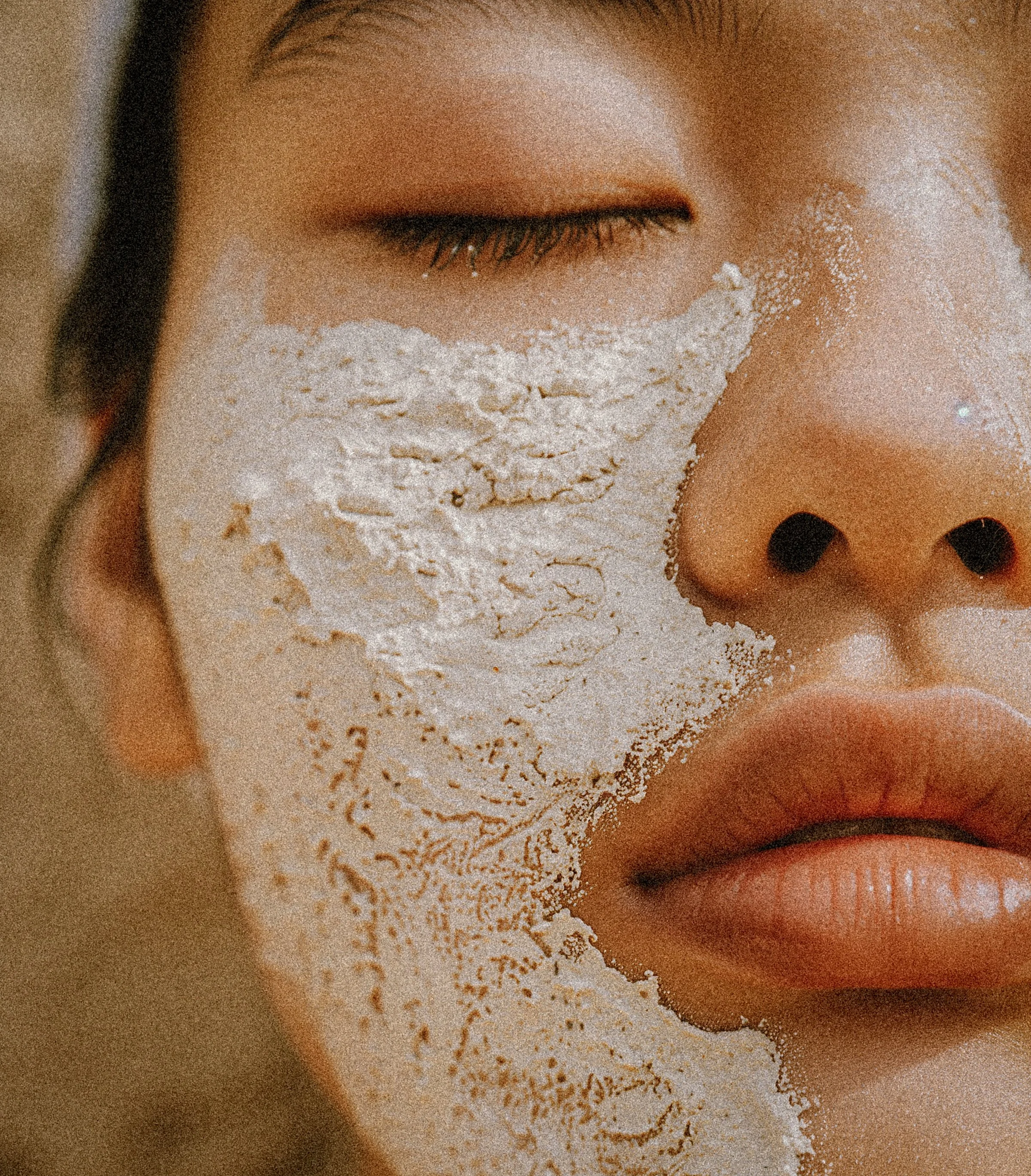 Close-up of a person's face with their eyes closed, and a white facial mask applied around the eyes, nose, and cheeks.