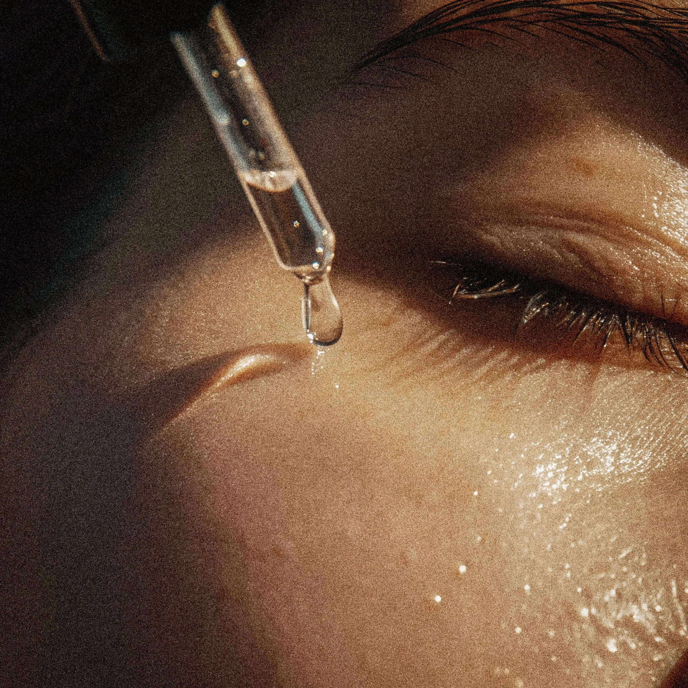 Close-up of a person's eye with water falling from a glass held above it, surrounded by shimmering light and wet skin.