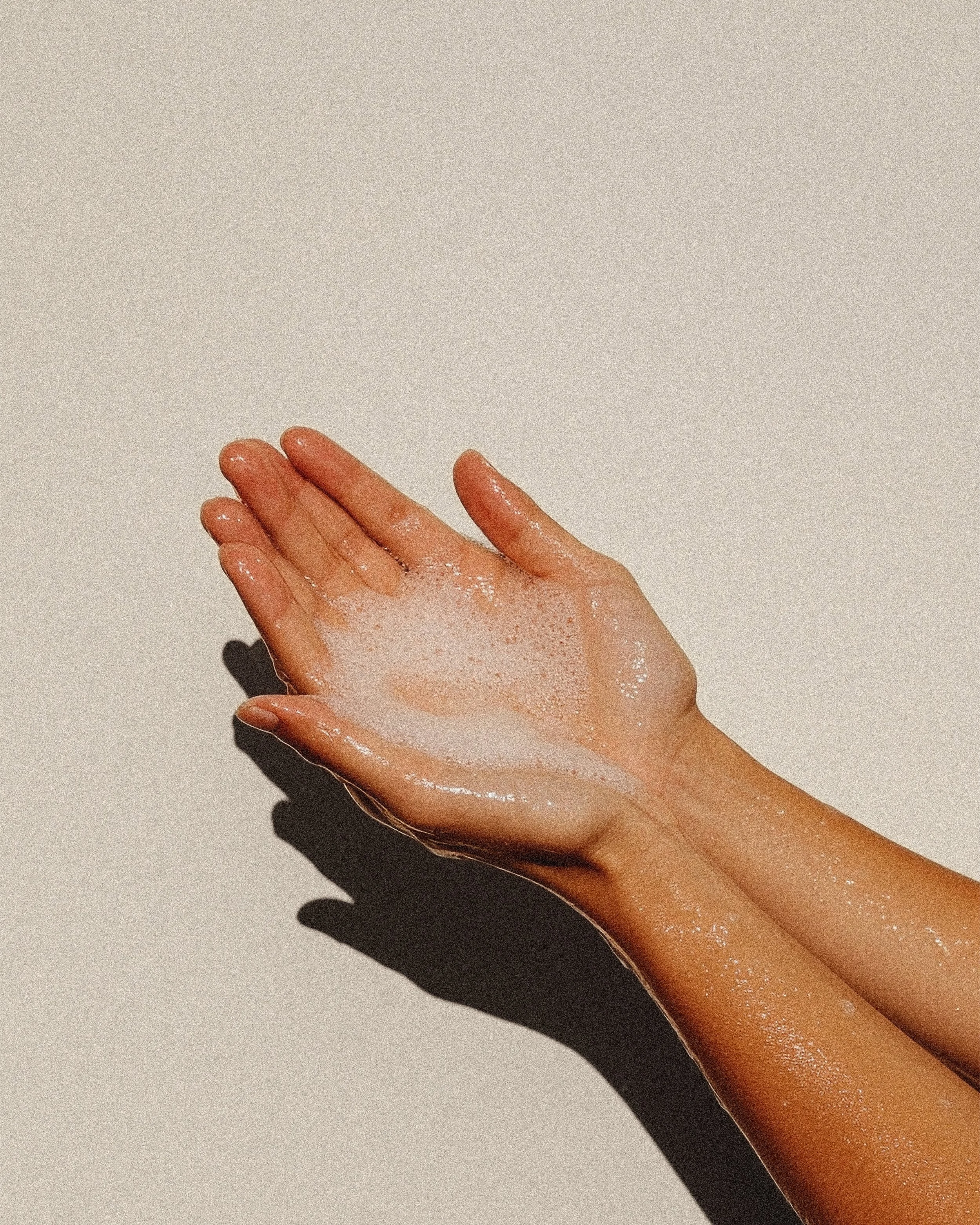 A close-up of a person's hand and forearm, covered in soap suds, against a plain light-colored background.