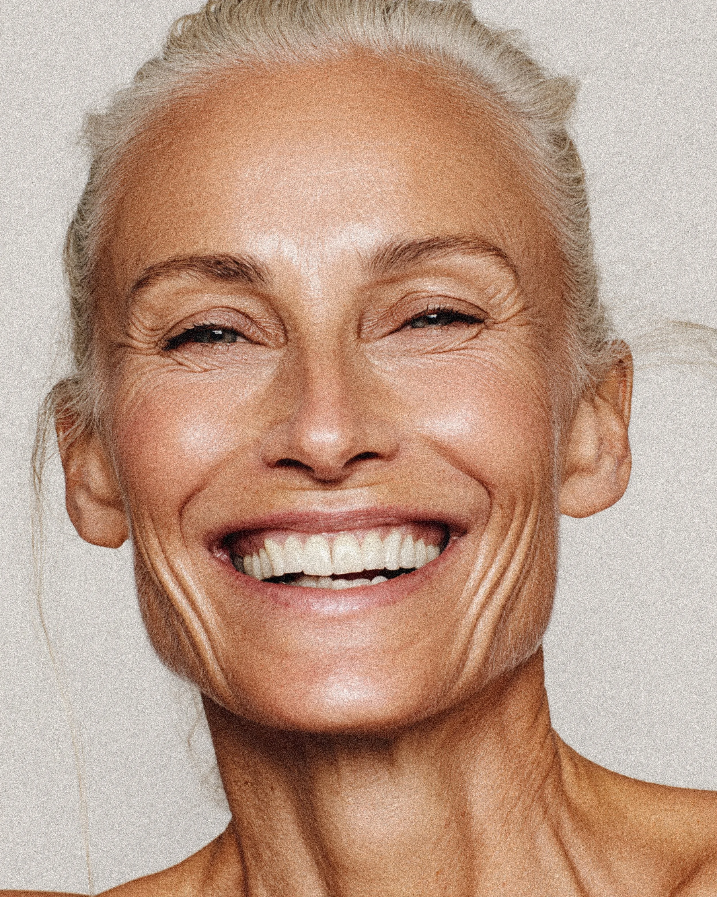 Close-up of an older woman's face with silver hair, smiling broadly, showing her teeth and crow's feet around her eyes.