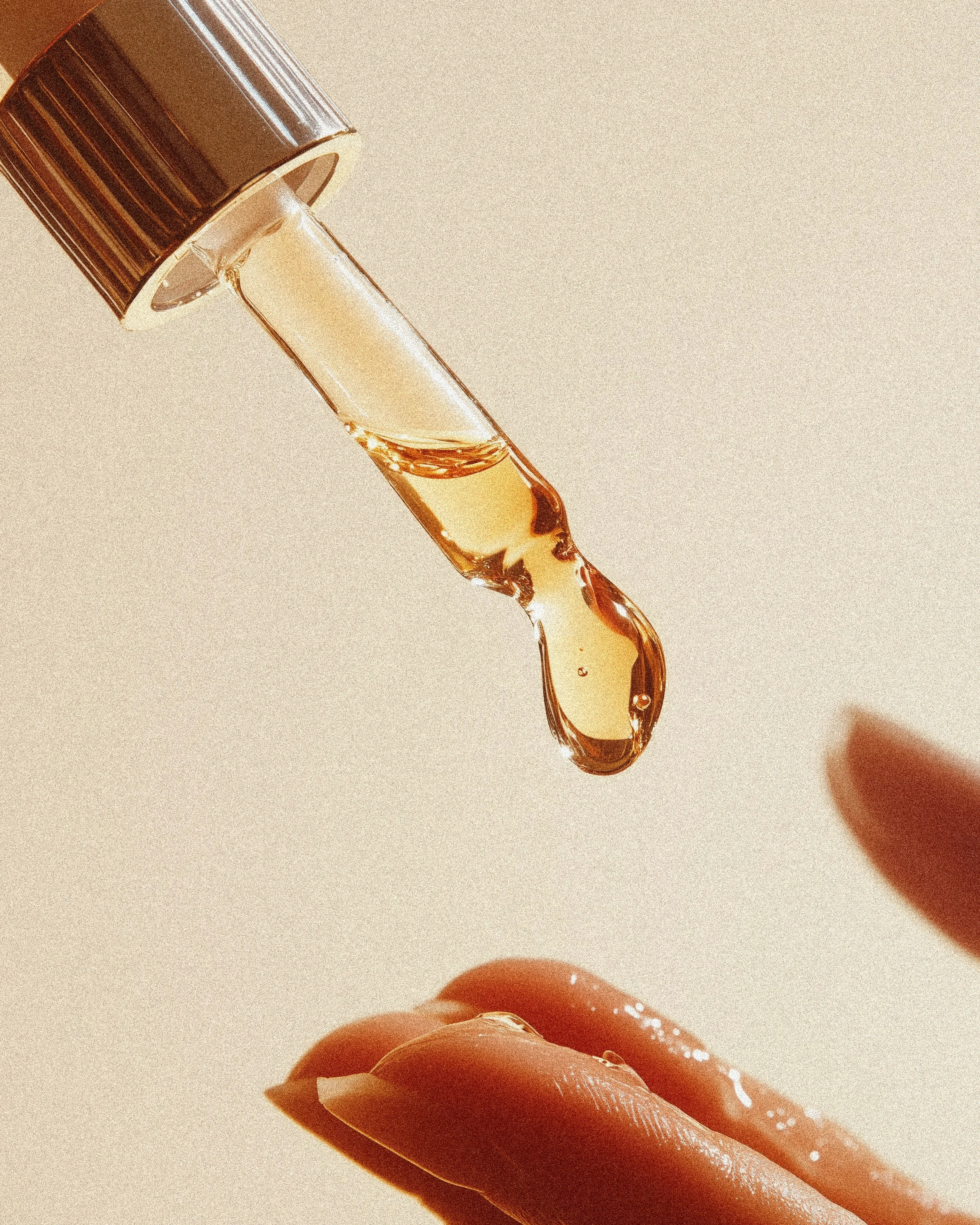 A hand holding a finger with a drop of honey being dripped from a honey dipper.