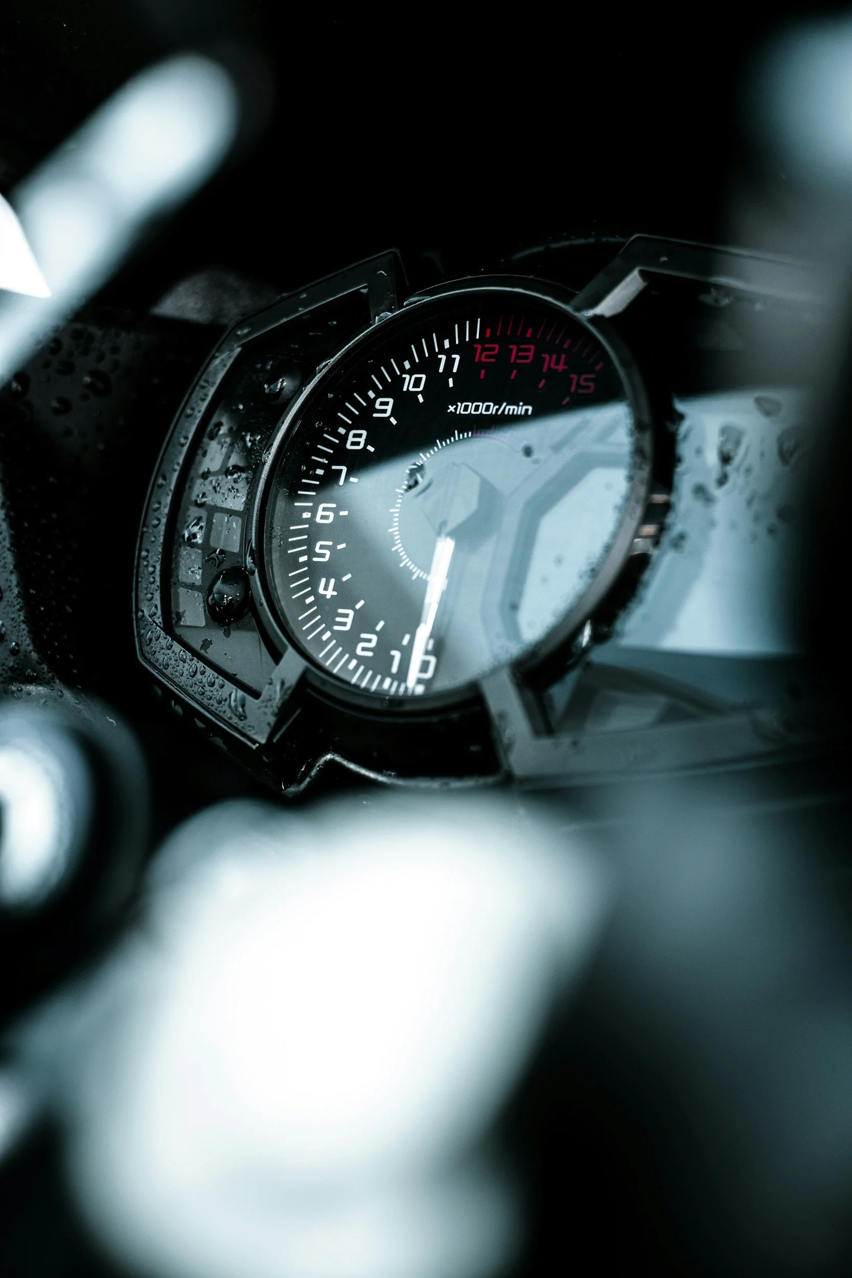 Close-up of a motorcycle tachometer with a digital display and water droplets on the surface.