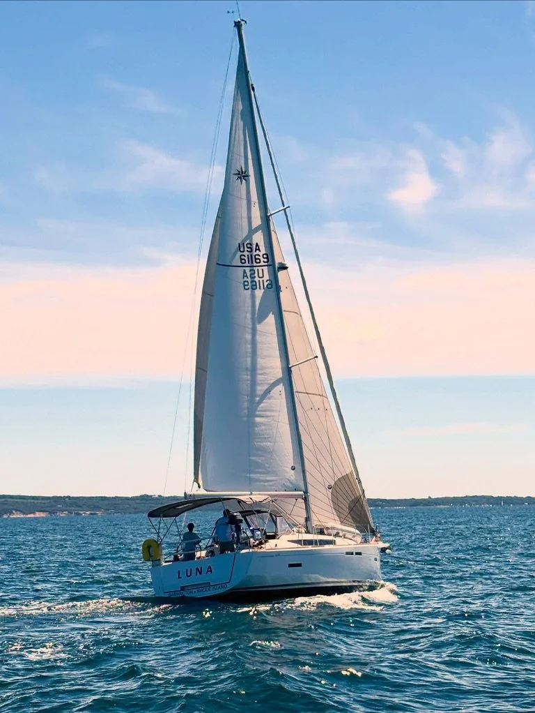 A white sailboat named Luna sailing on the ocean under a partly cloudy sky.