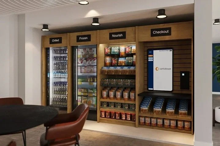 A self-serve vending area with sections labeled Chilled, Frozen, Nourish, and Checkout, containing drinks, frozen foods, snacks, and a digital checkout screen.