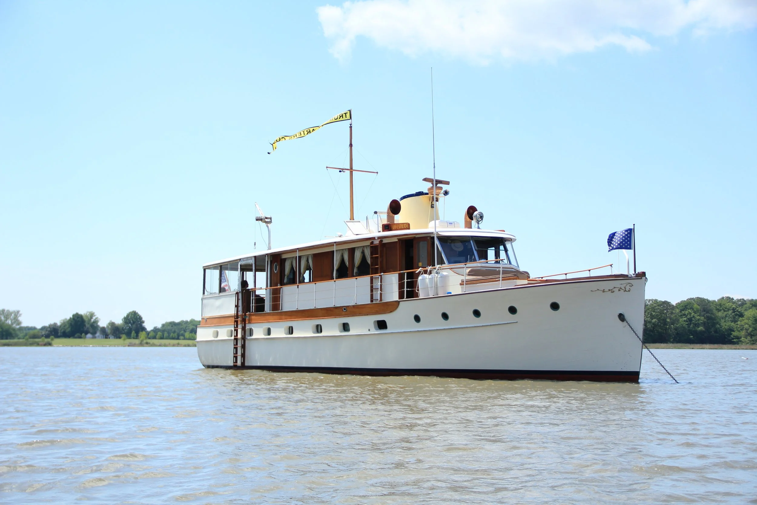 A vintage Trumpy Yacht sitting anchored on a river on a sunny day.