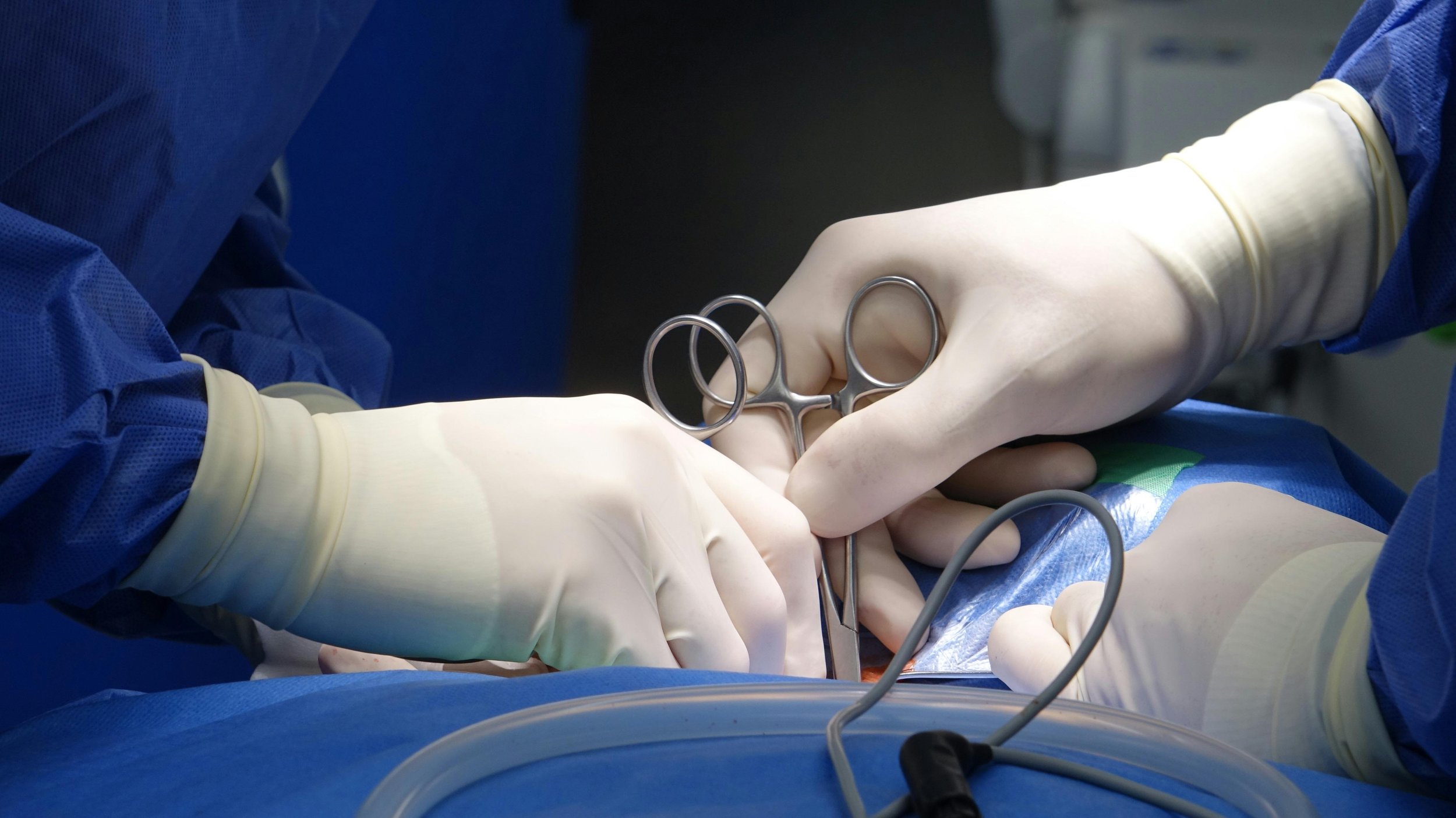 Spine surgeons in sterile gloves and gowns performing a surgical procedure using surgical scissors.