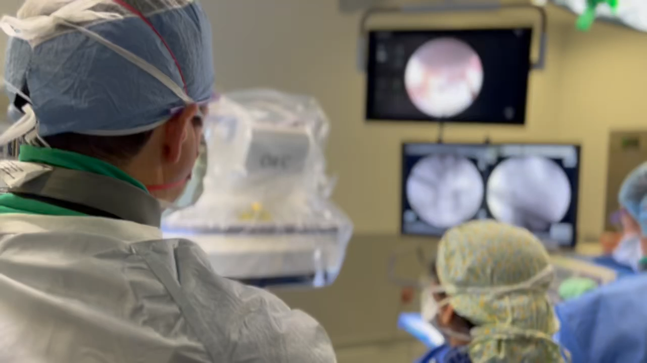 Spine surgeons in an operating room performing a minimally invasive procedure while viewing monitors displaying medical images.