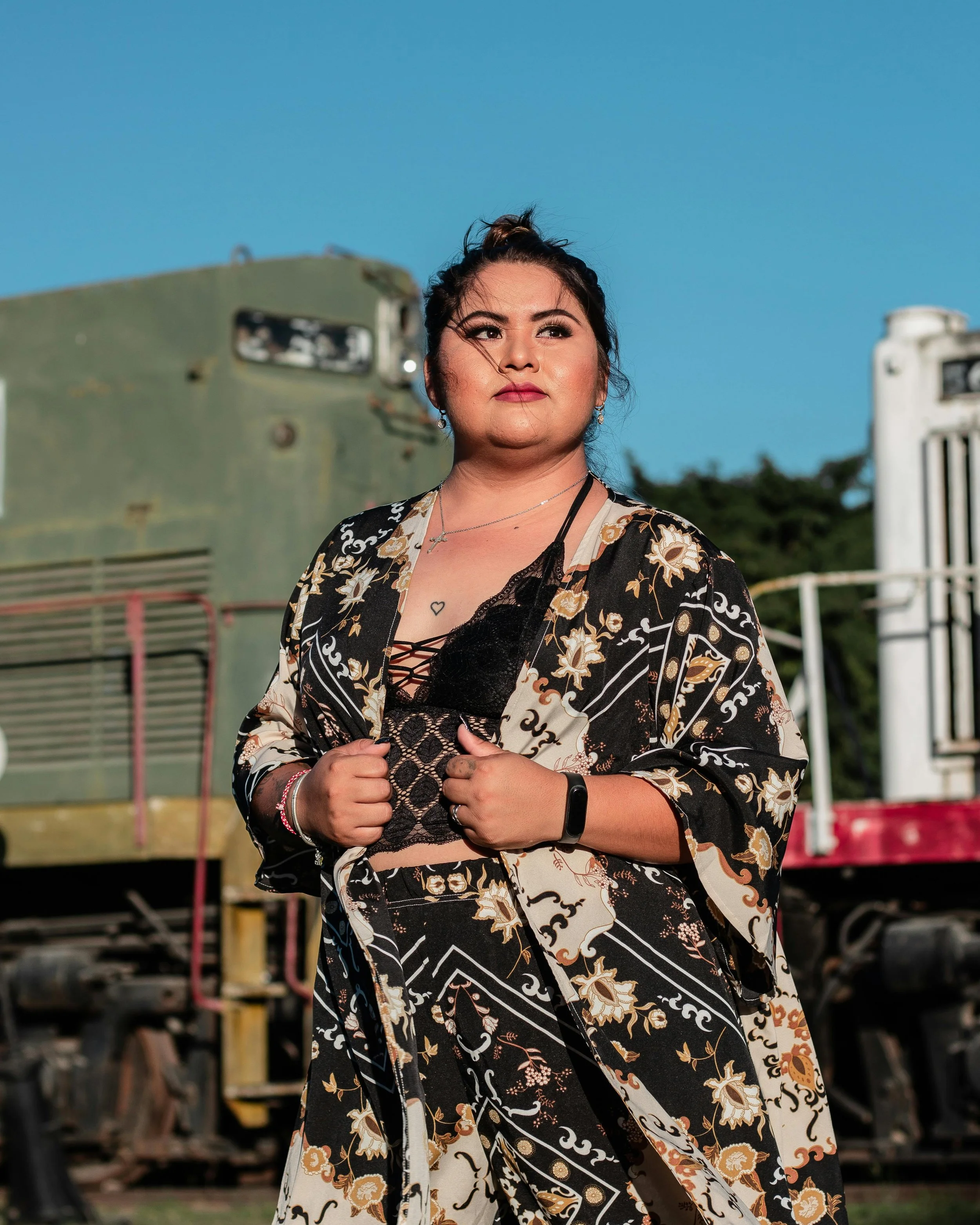 A woman standing outdoors in a floral kimono-style outfit against a green backdrop, symbolizing identity exploration and authenticity.