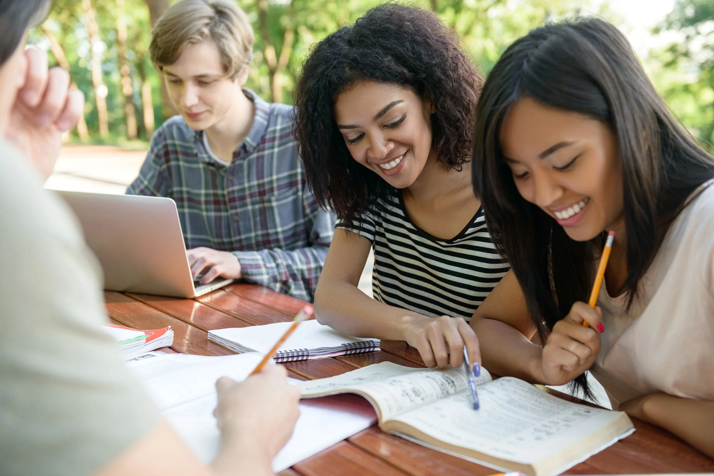 A diverse group of four college students collaborating outdoors with notebooks and pens, representing support for young adult populations