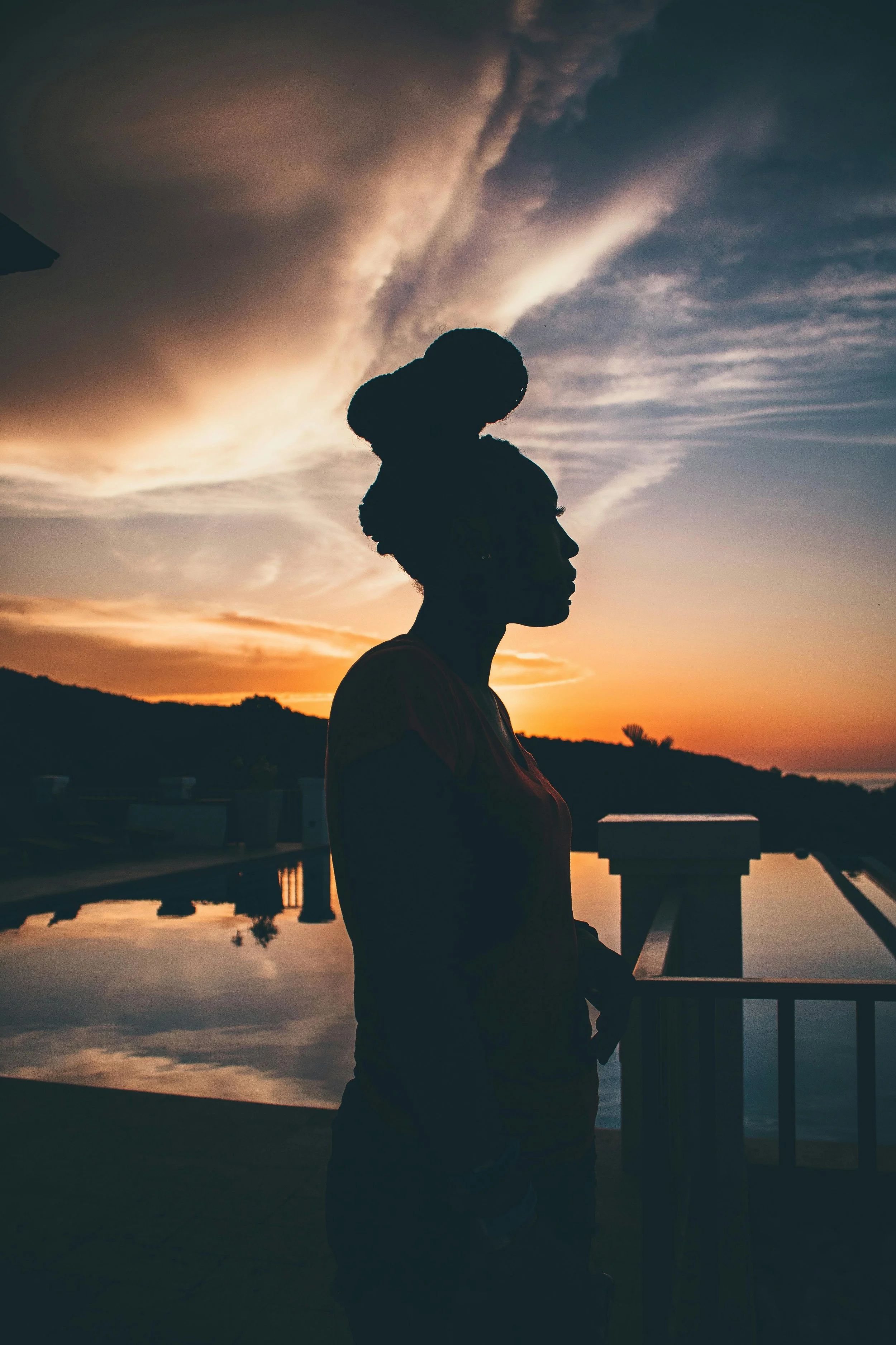 Black woman admiring sea near mountain at colorful sunset, a demographic queer black woman therapist Dr. Mary Woodson frequently helps with trauma and PTSD.