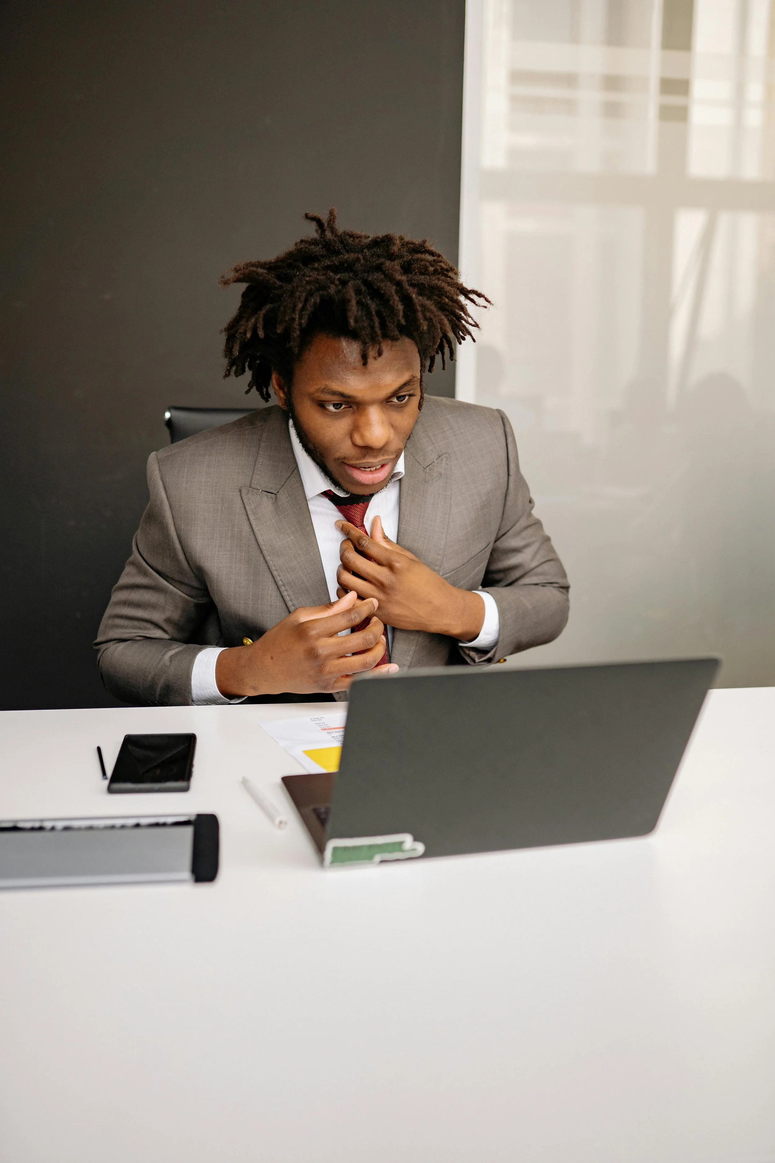 A Black man professional in a gray suit and red tie sitting at a modern desk with a laptop, highlighting services for high-achieving professionals
