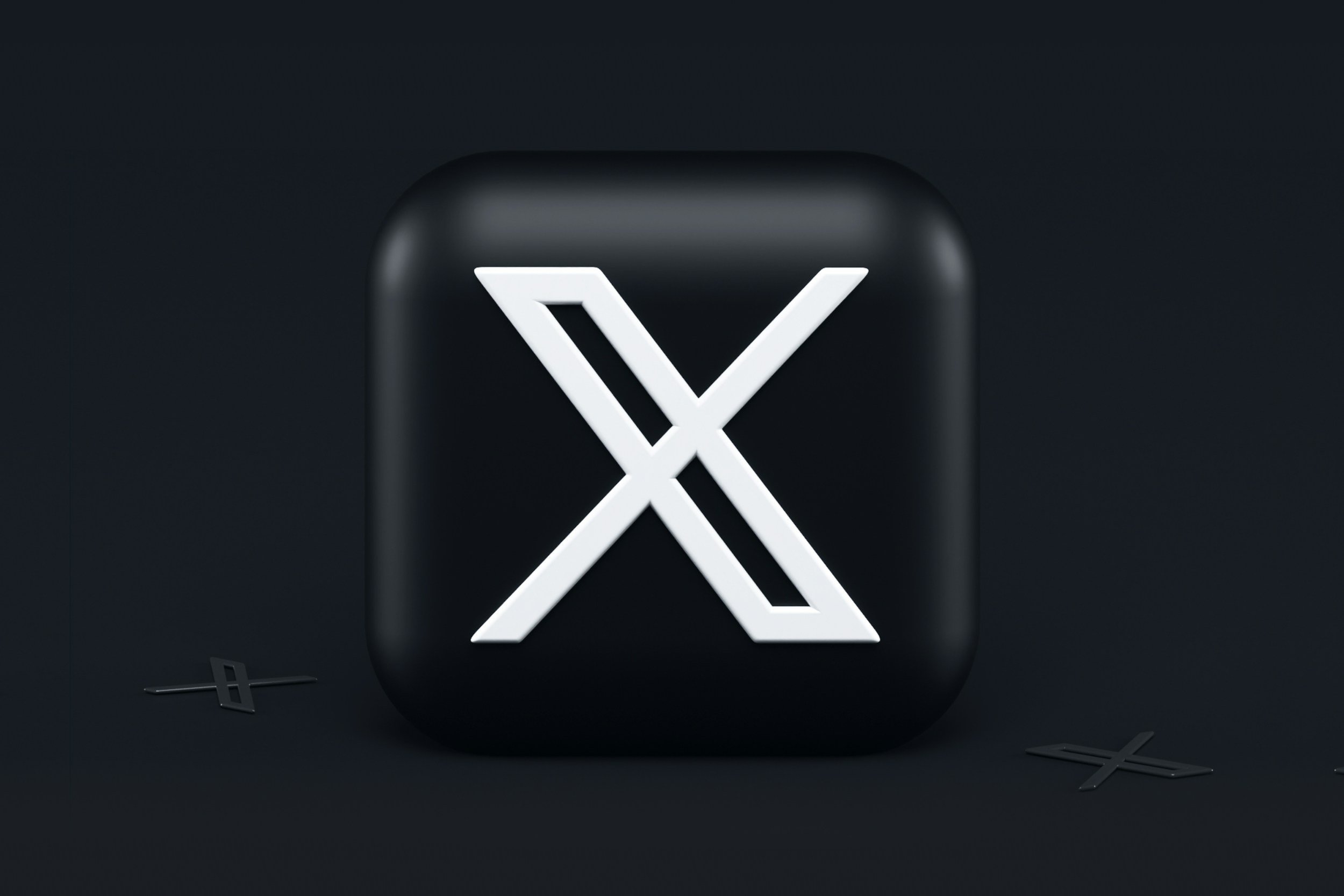 A black square button with rounded edges and a white stylized 'X' design in the center, surrounded by small black 'X' shapes on a dark background.