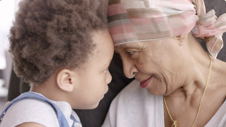 A young child and an elderly woman with a headscarf touching foreheads, sharing a tender moment.