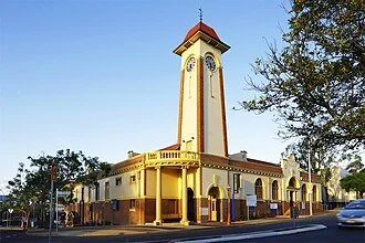 A historic building with a tall clock tower, yellow and white exterior, surrounded by trees and cars on the street.