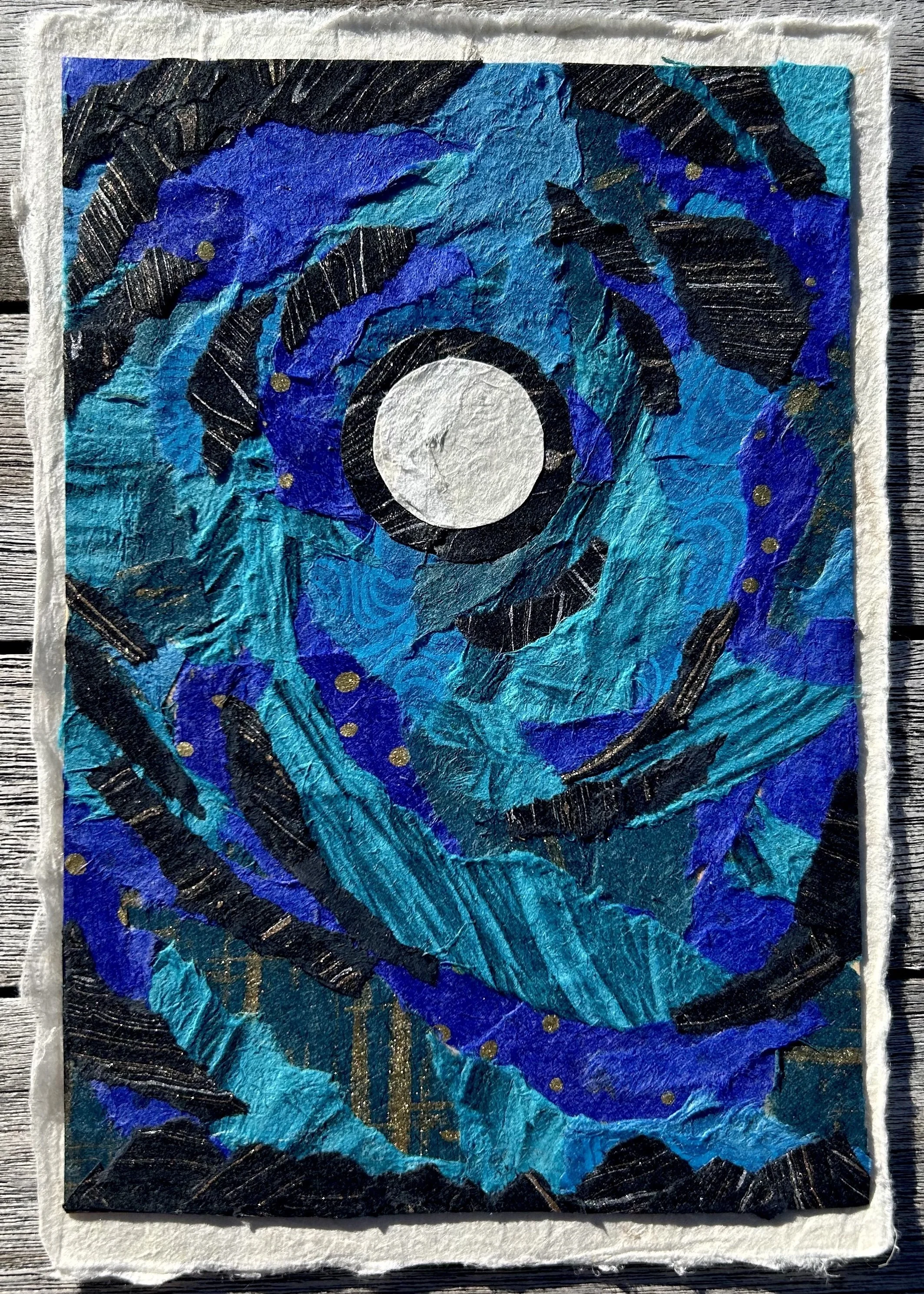 An abstract mixed-media artwork featuring swirling shades of blue, black, and gold, with a central white circle and a textured background.