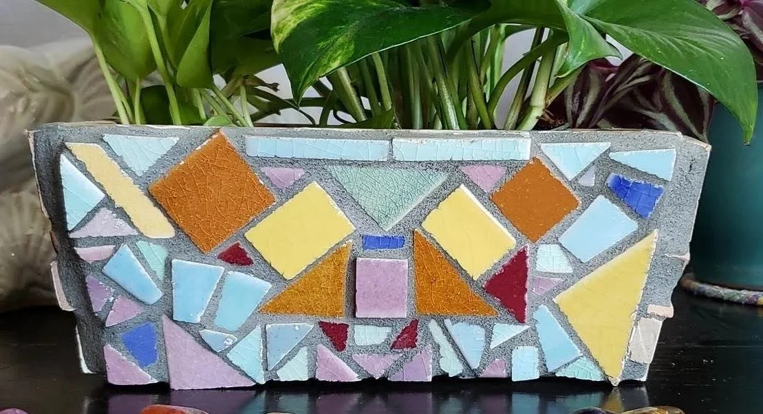 A colorful mosaic planter with plants in the background.