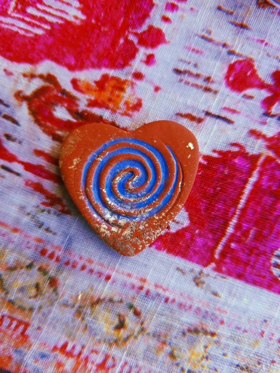 Heart-shaped cookie with a blue spiral decoration on a colorful fabric background.