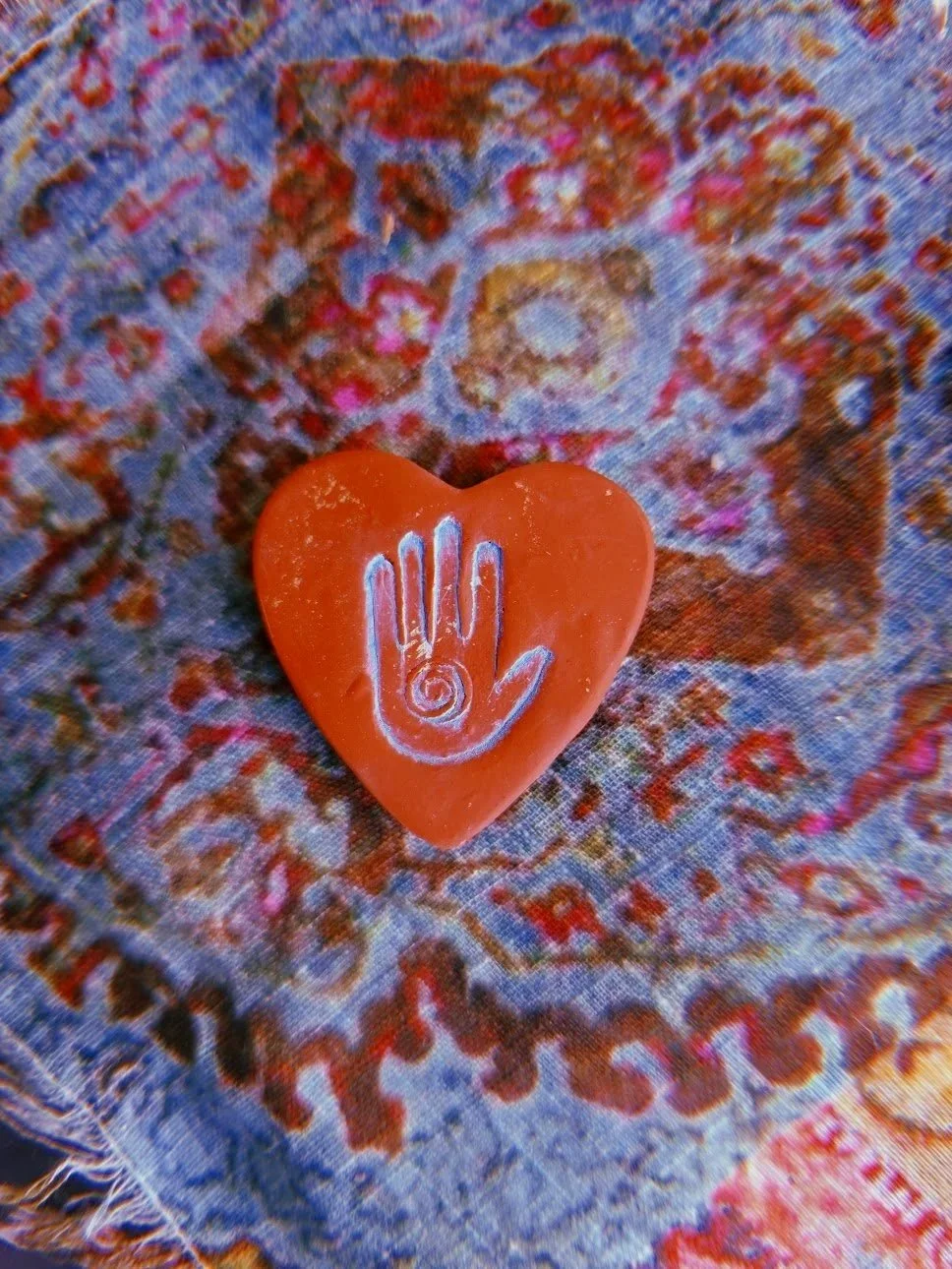 A red heart-shaped object with a white handprint design on it, placed on a colorful patterned fabric background.