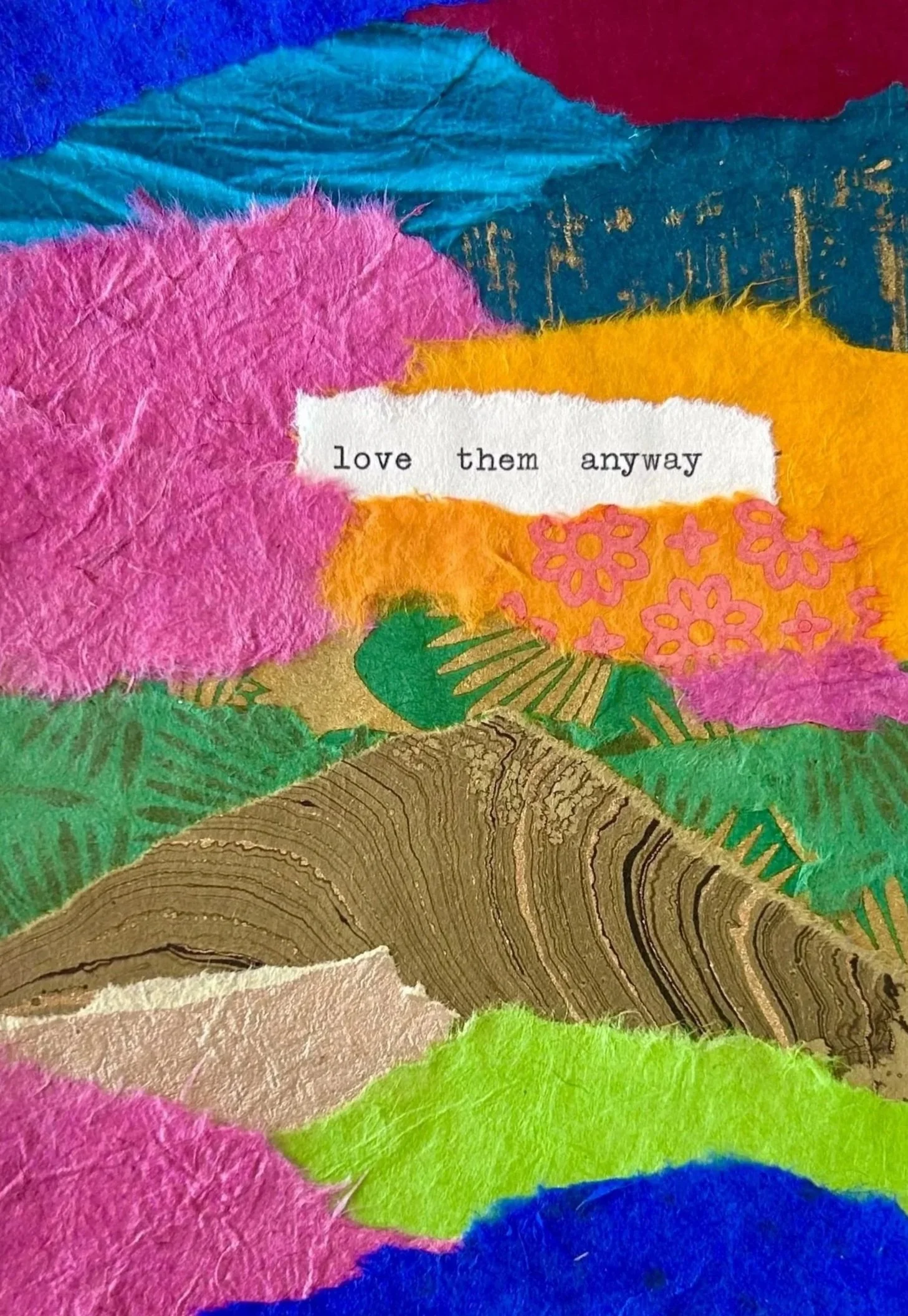 A colorful collage made of torn paper with mountains and trees in pink, blue, green, yellow, orange, brown, and gold, featuring a torn white paper with the words 'love them anyway' printed on it.