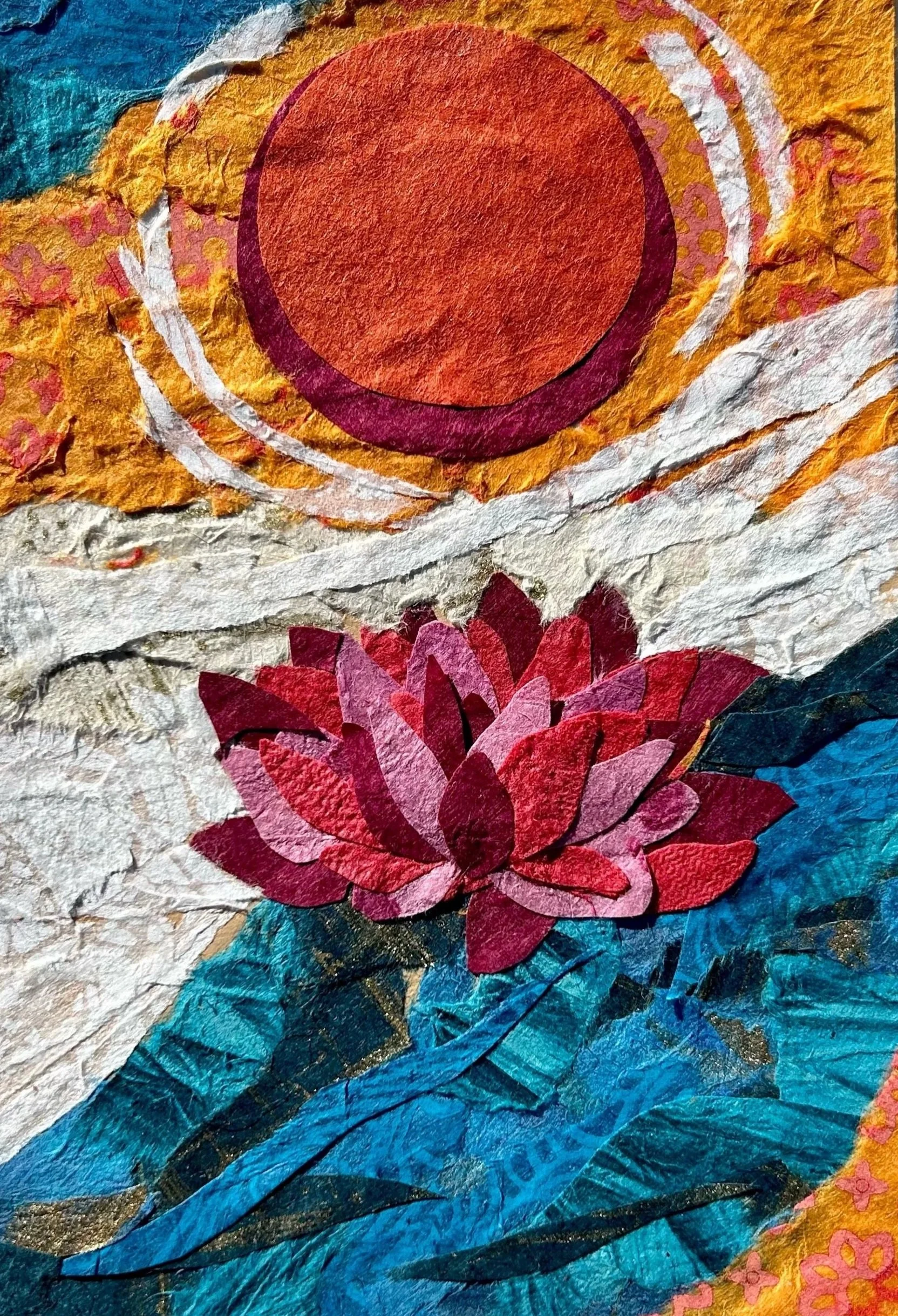 A collage artwork made from torn paper depicting a sunset, a pink and red lotus flower on blue water, and a background with orange, yellow, and pink colors.