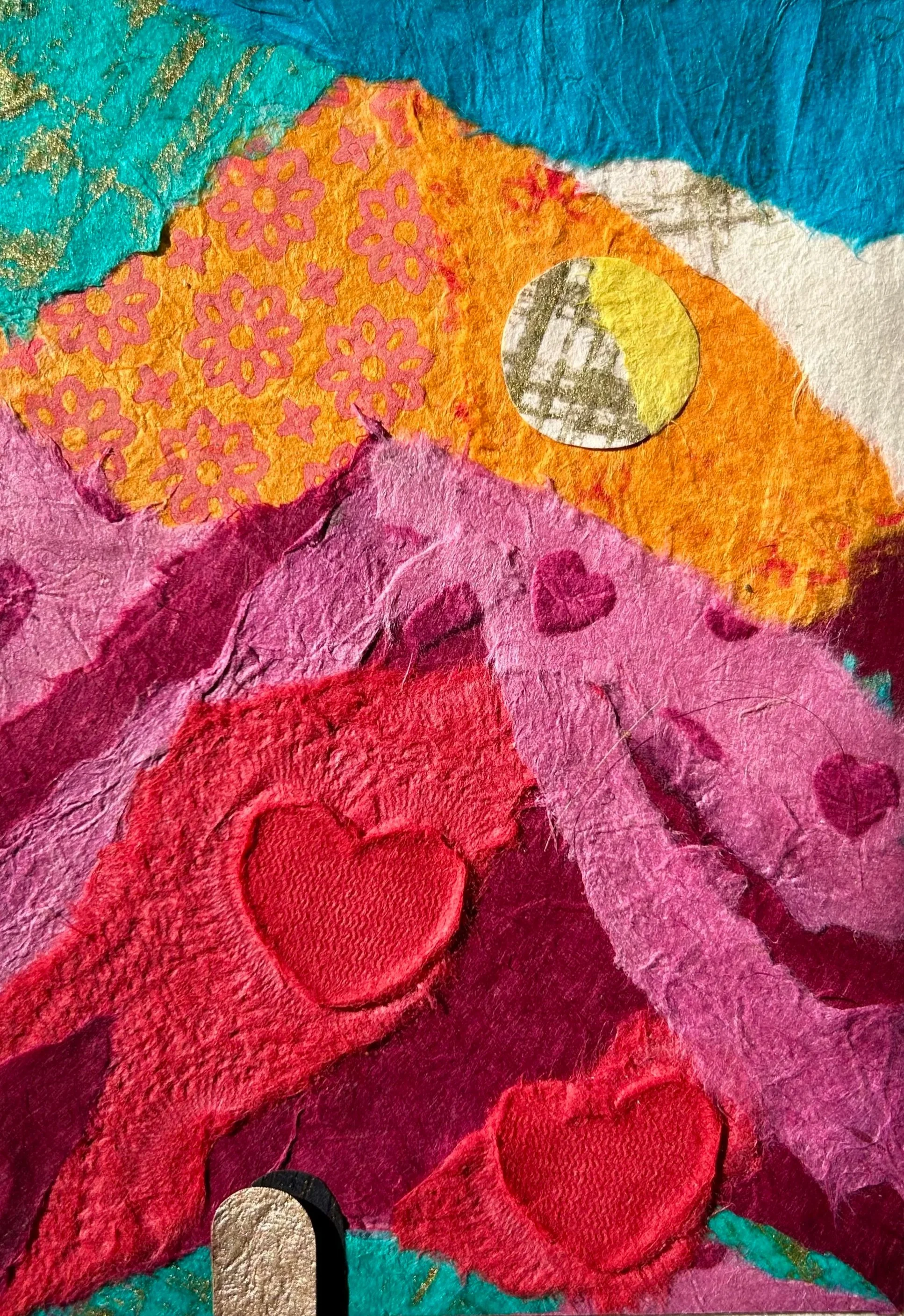 A colorful collage art piece featuring mountains, hearts, a moon, clouds, and a star, made from textured paper and fabric.