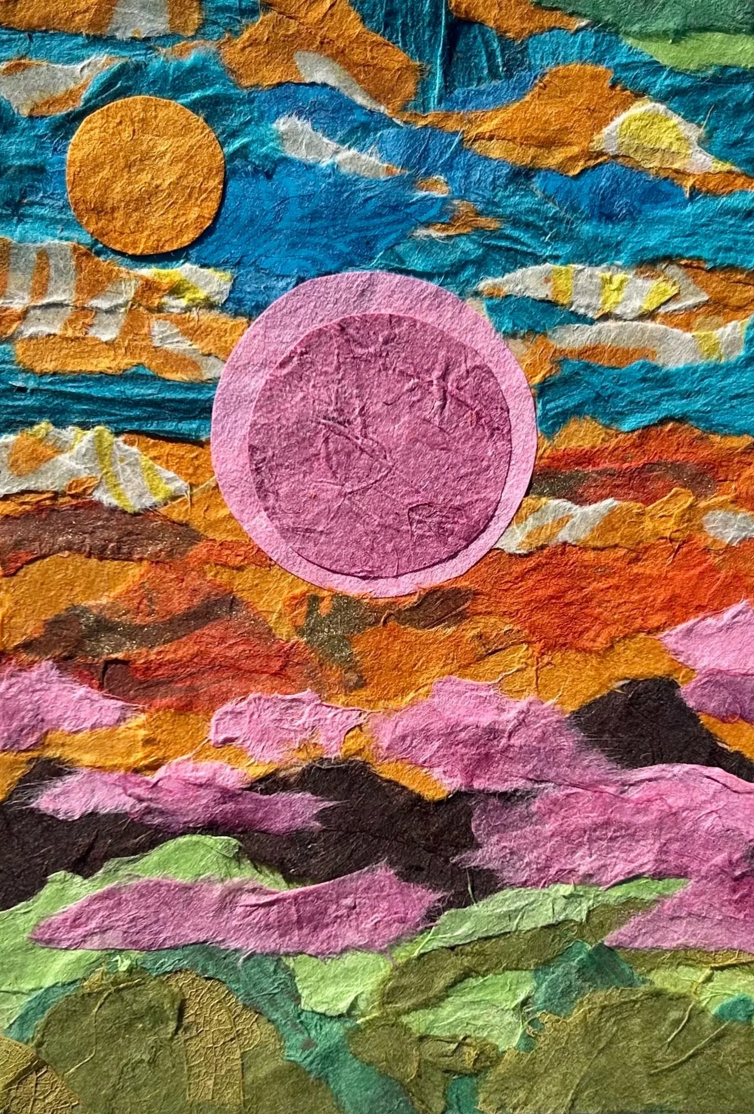 A colorful collage of torn paper creating a landscape scene with a sky, mountains, and a prominent pink circle and yellow-orange sun.