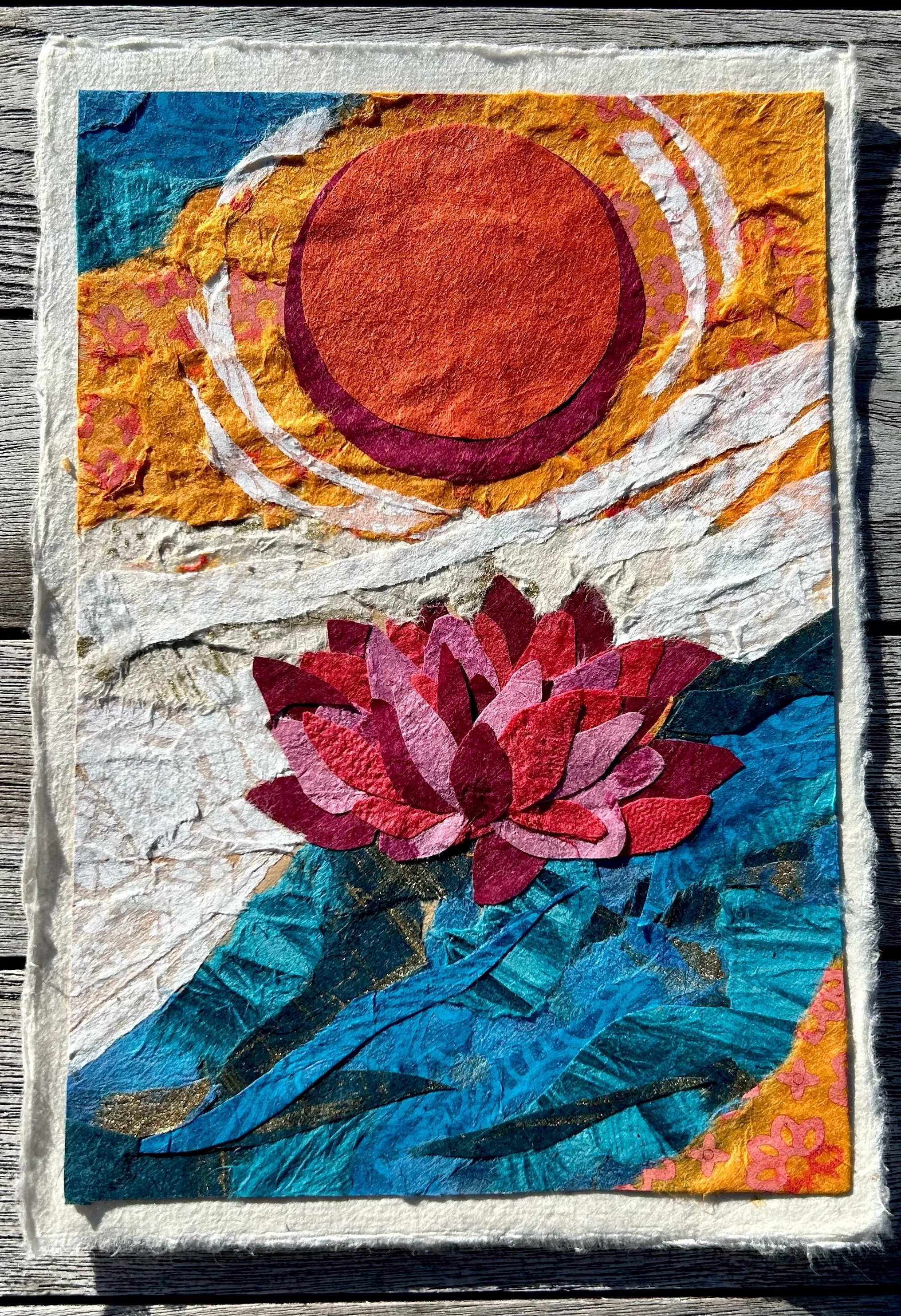 A collage artwork made from torn paper depicting a sunset, a pink and red lotus flower on blue water, and a background with orange, yellow, and pink colors.