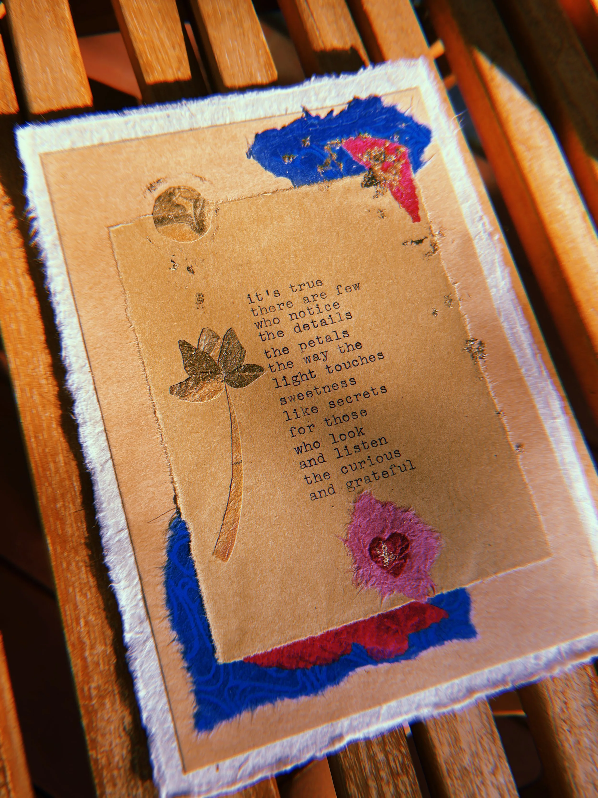 A textured piece of art with embroidered and painted elements featuring a poem about appreciating small details, flowers, and secrets, placed on a wooden surface.