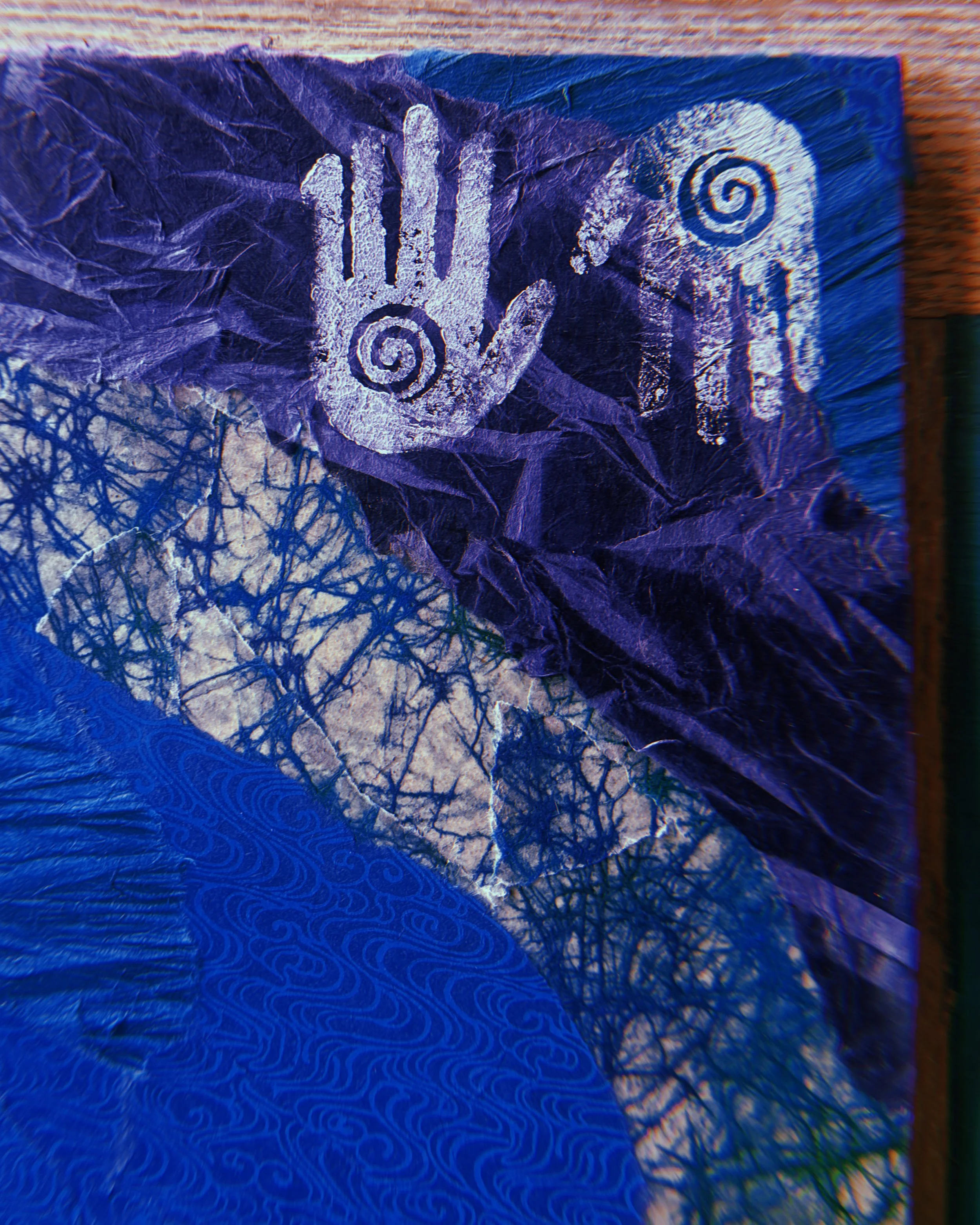 Close-up of a textured, crumpled blue and purple paper with white handprints and spiral designs.