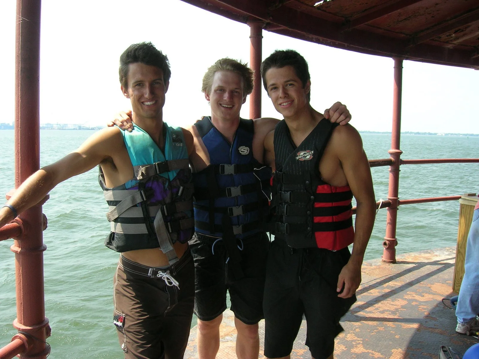 Three young men standing on Middle Ground Lighthouse, all wearing life jackets and smiling.